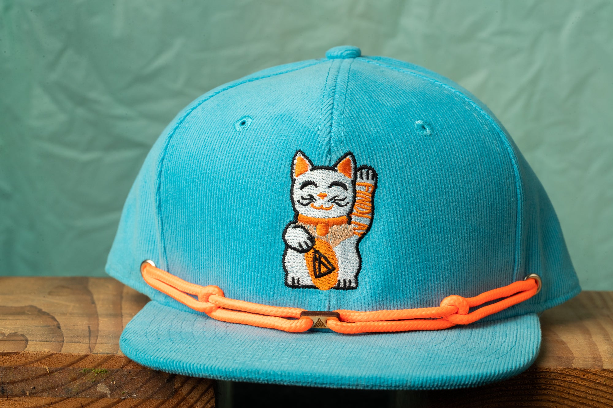 A turquoise baseball cap with an embroidered cat design on the front.