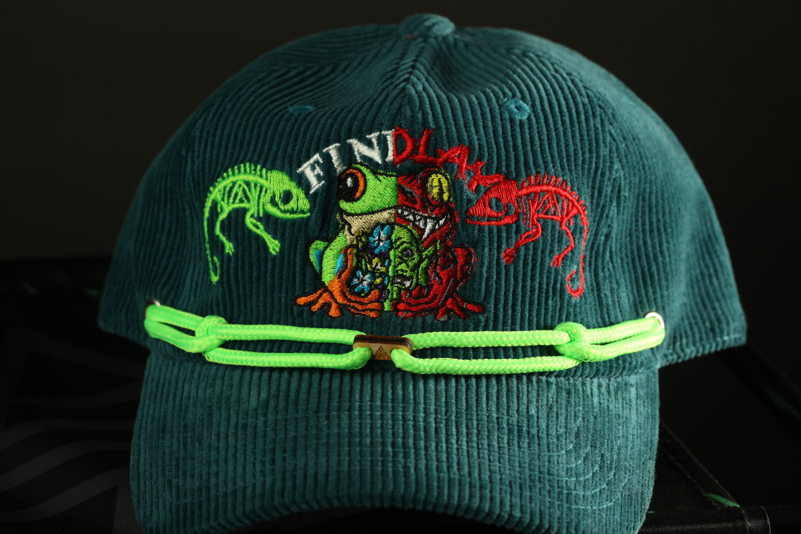 A close-up image of a green baseball cap with a frog design and the word "FIND" printed on it.