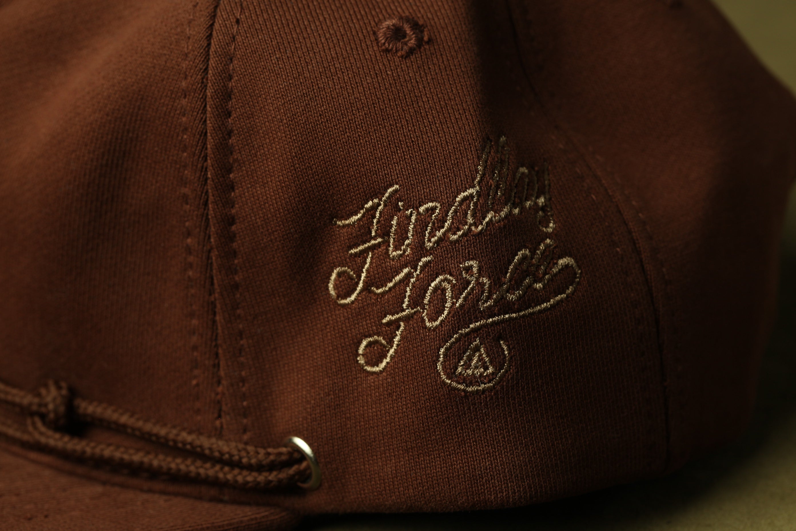 A close-up view of a brown baseball cap with embroidered text on the side.