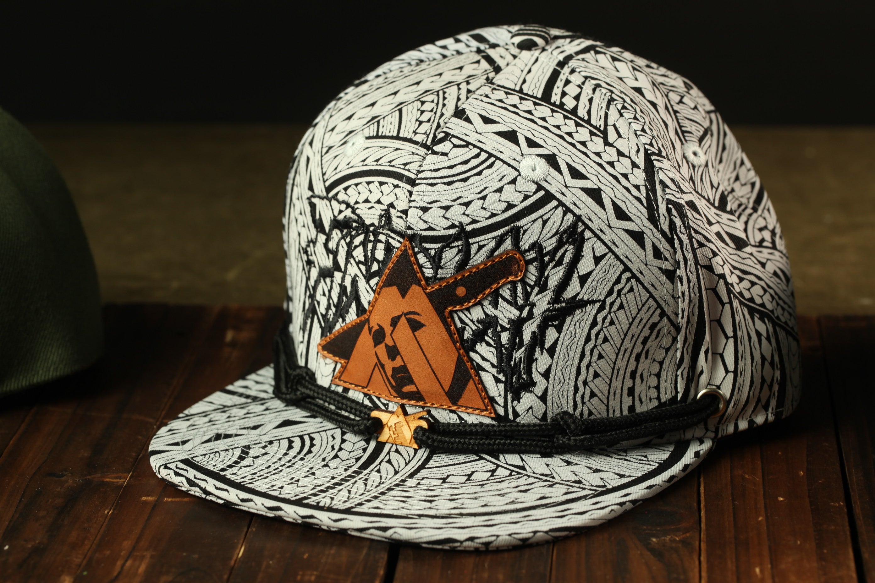 A black and white patterned baseball cap with a distinctive orange triangle logo on the front, resting on a wooden surface.