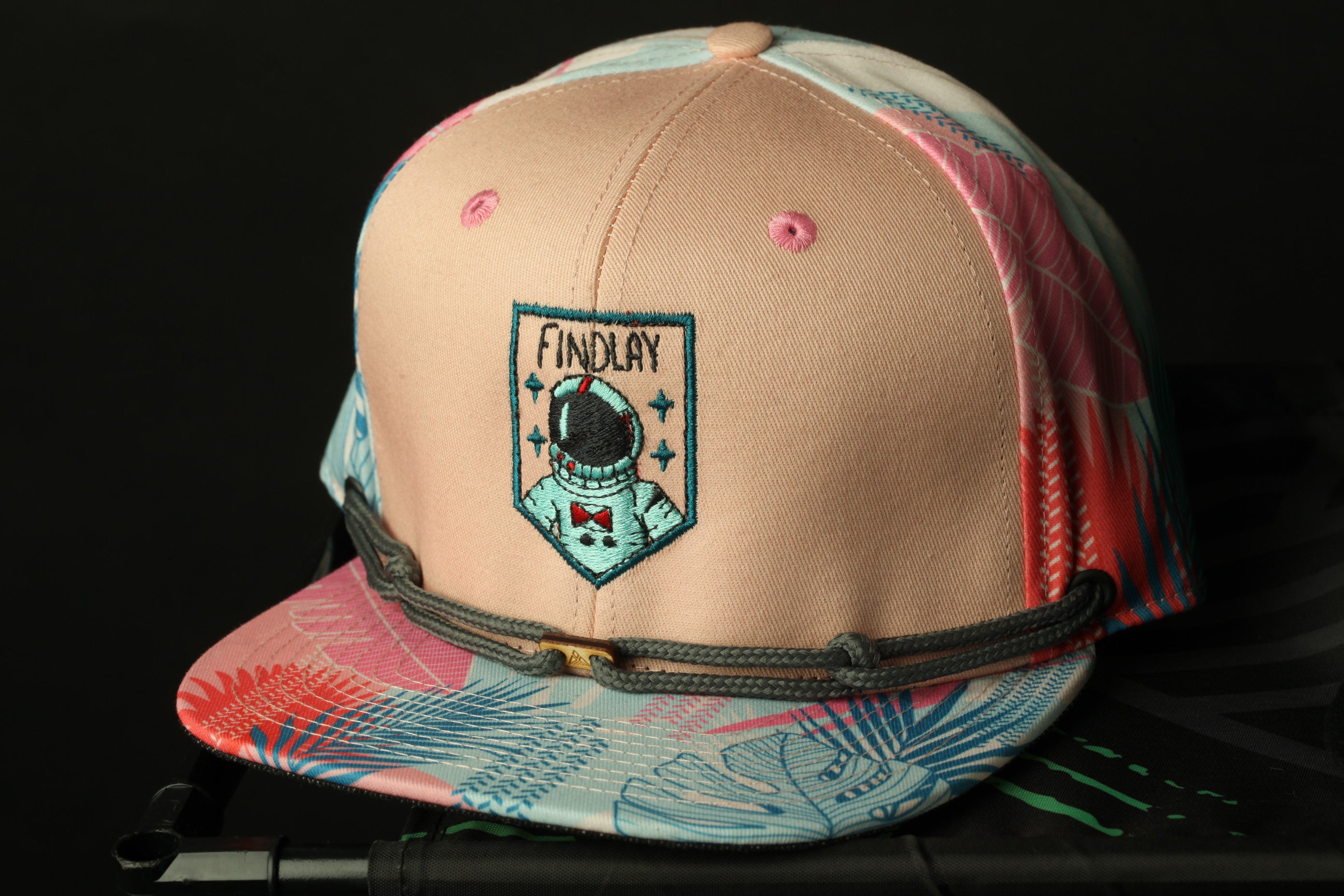A pink baseball cap with a graphic of an astronaut and the word "FINDLAY" on it, along with a floral pattern.