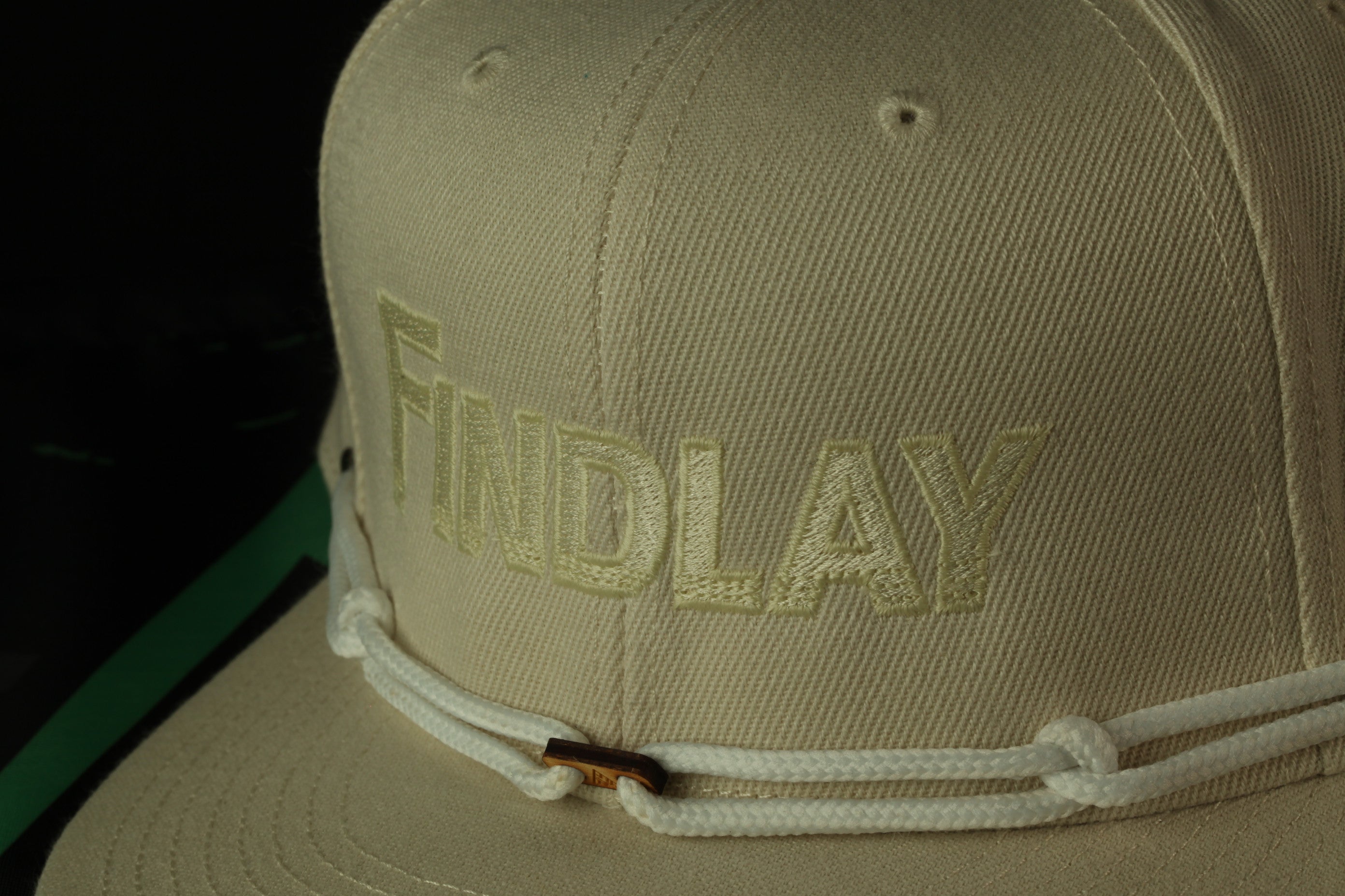 A close-up view of a beige baseball cap with the word "Findlay" embroidered on it.
