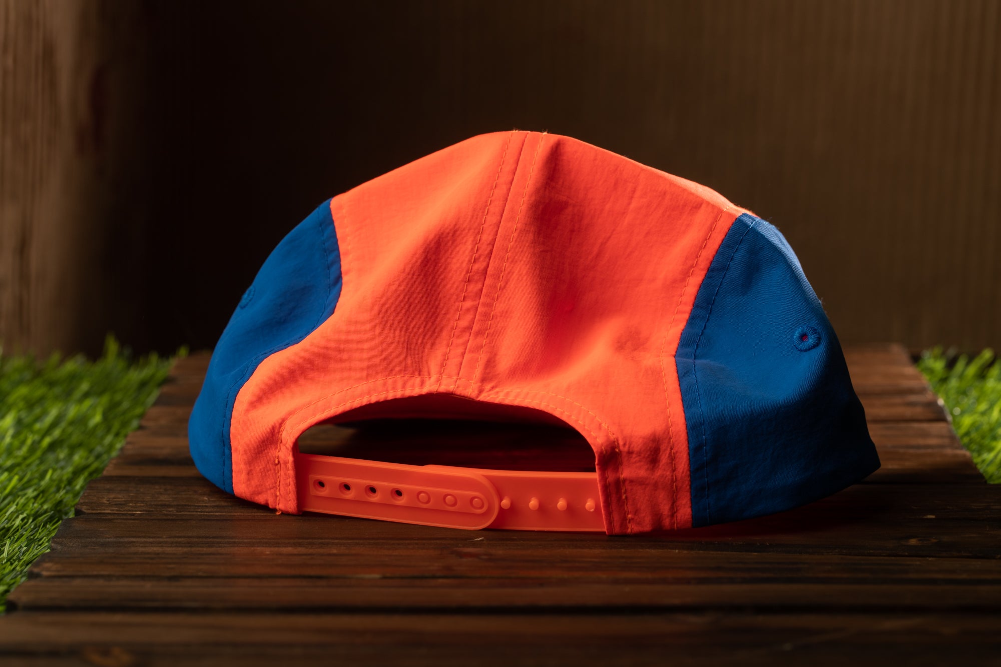A red and blue baseball cap is placed on a wooden surface, with a grassy area visible in the background.