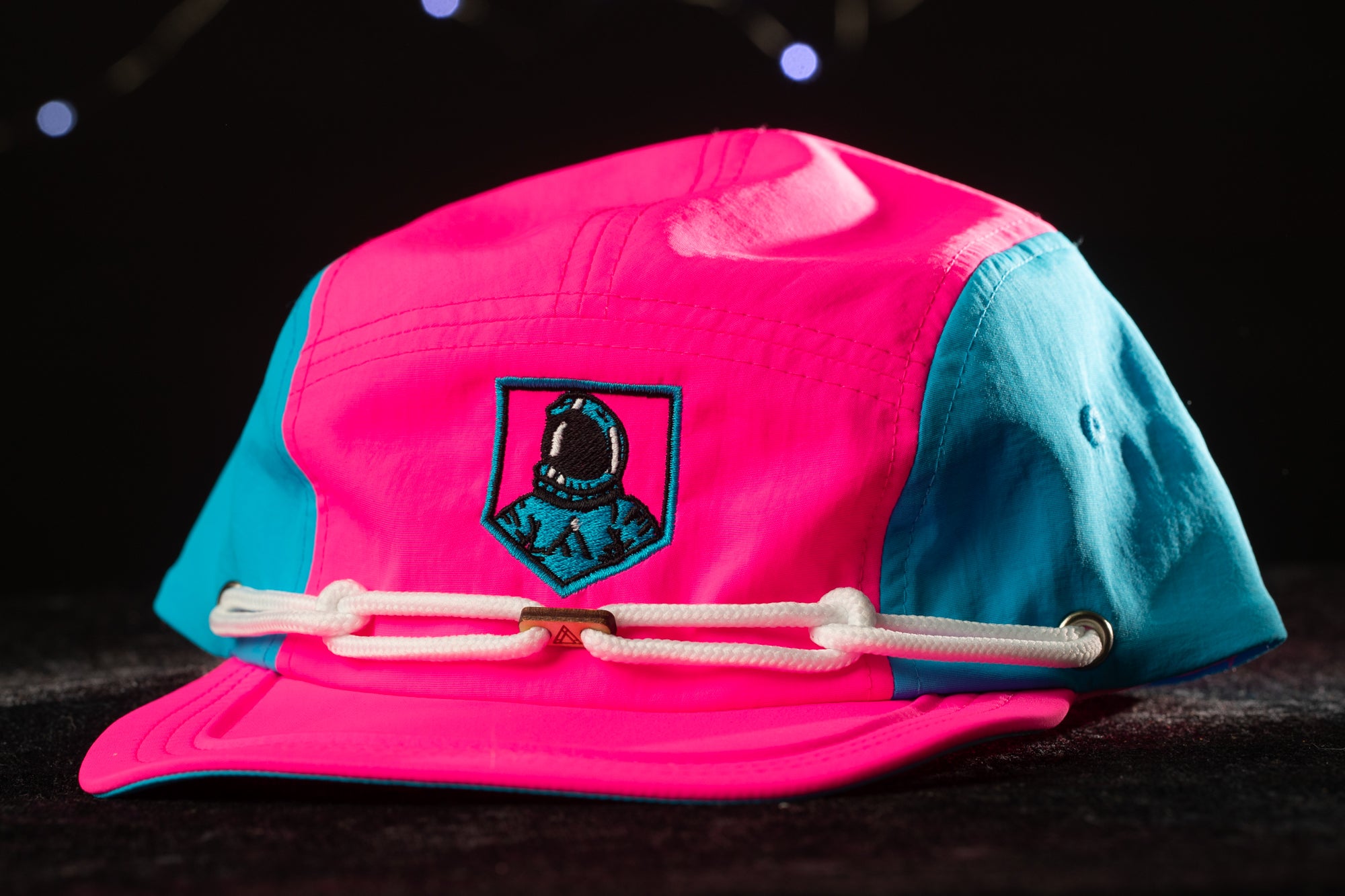 A bright pink and blue baseball cap with a small embroidered patch featuring a person's face.