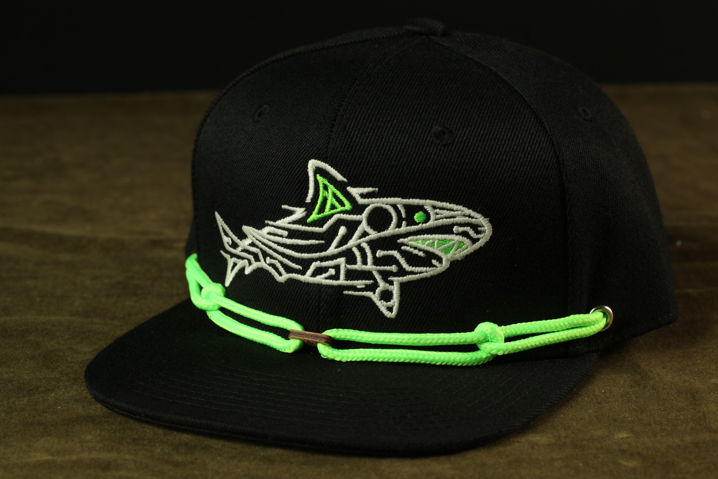 A black baseball cap with a white and green embroidered shark design on the front.