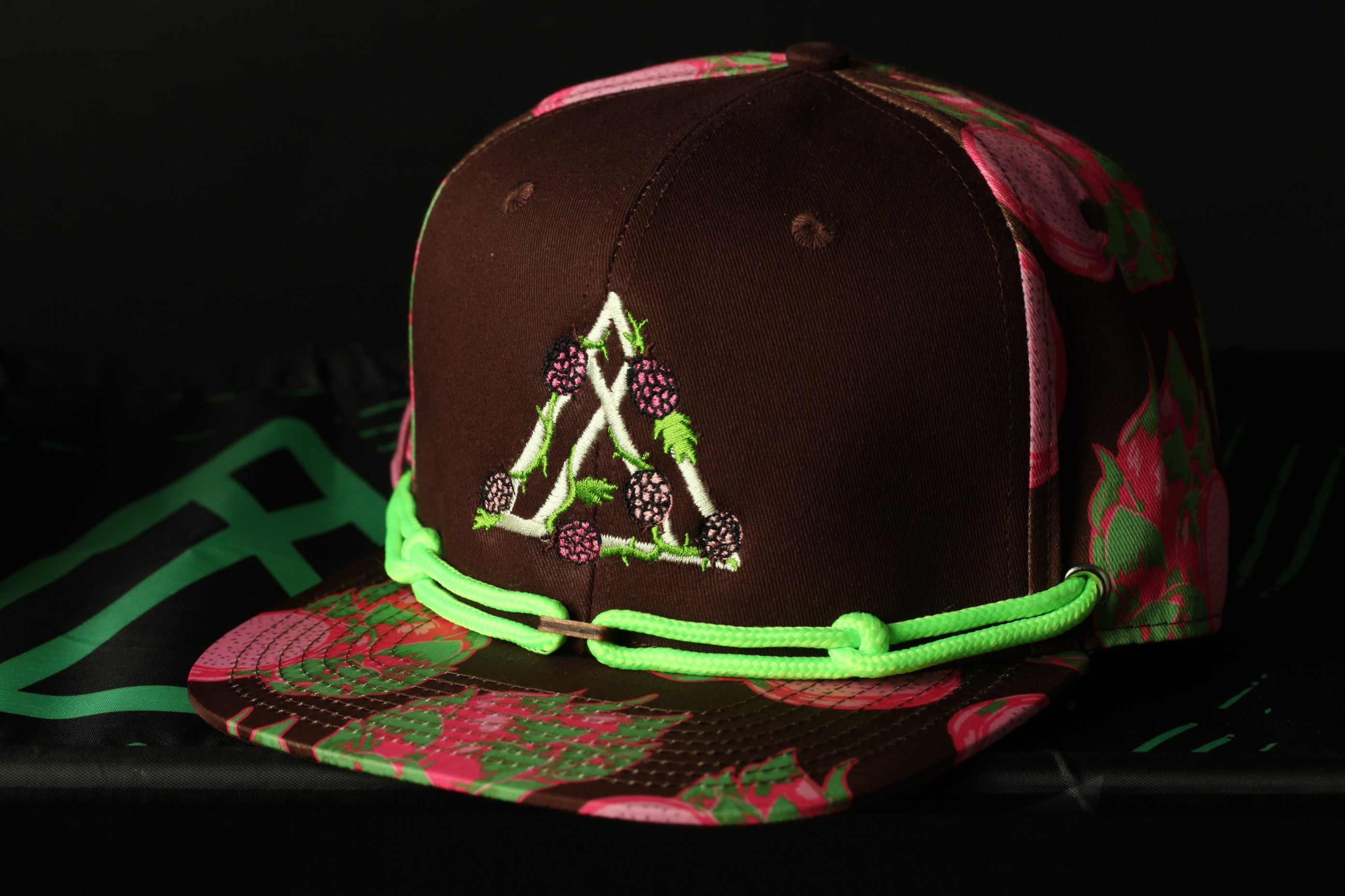 A brown baseball cap with a floral pattern and a triangle design on the front, featuring green strings.