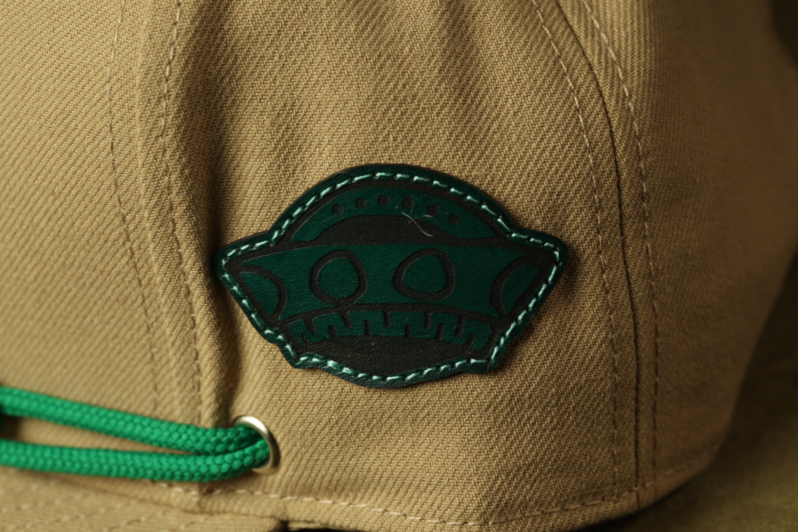 A close-up view of a beige fabric with a green embroidered logo on it.