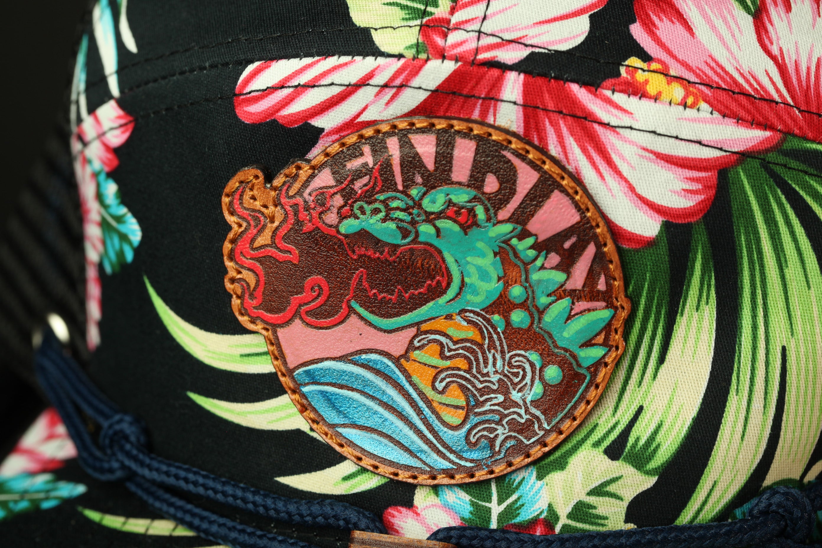 A close-up view of a colorful, floral-patterned hat with a circular patch featuring a dragon design.