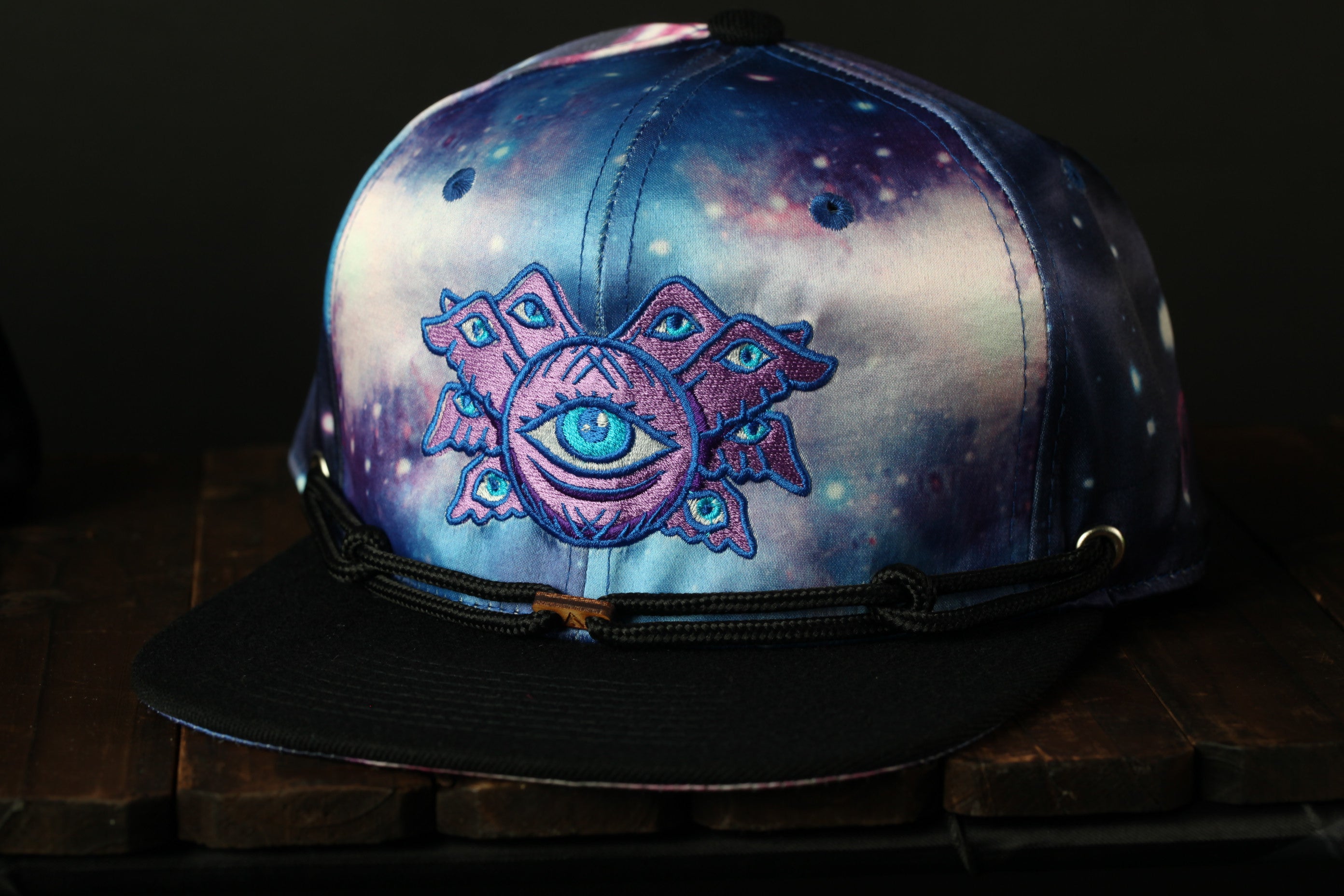 A colorful, patterned baseball cap with an eye design on the front, sitting on a wooden surface.