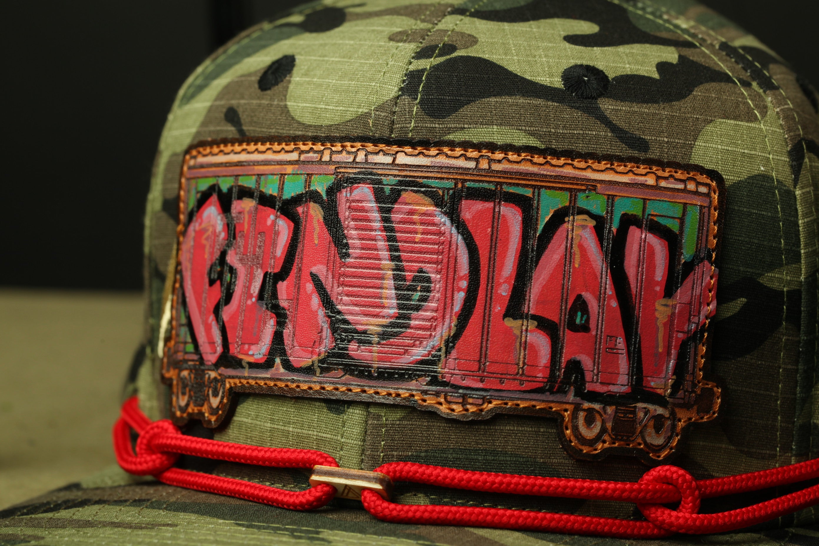 A camouflage baseball cap with a red and black graffiti-style design on the front.