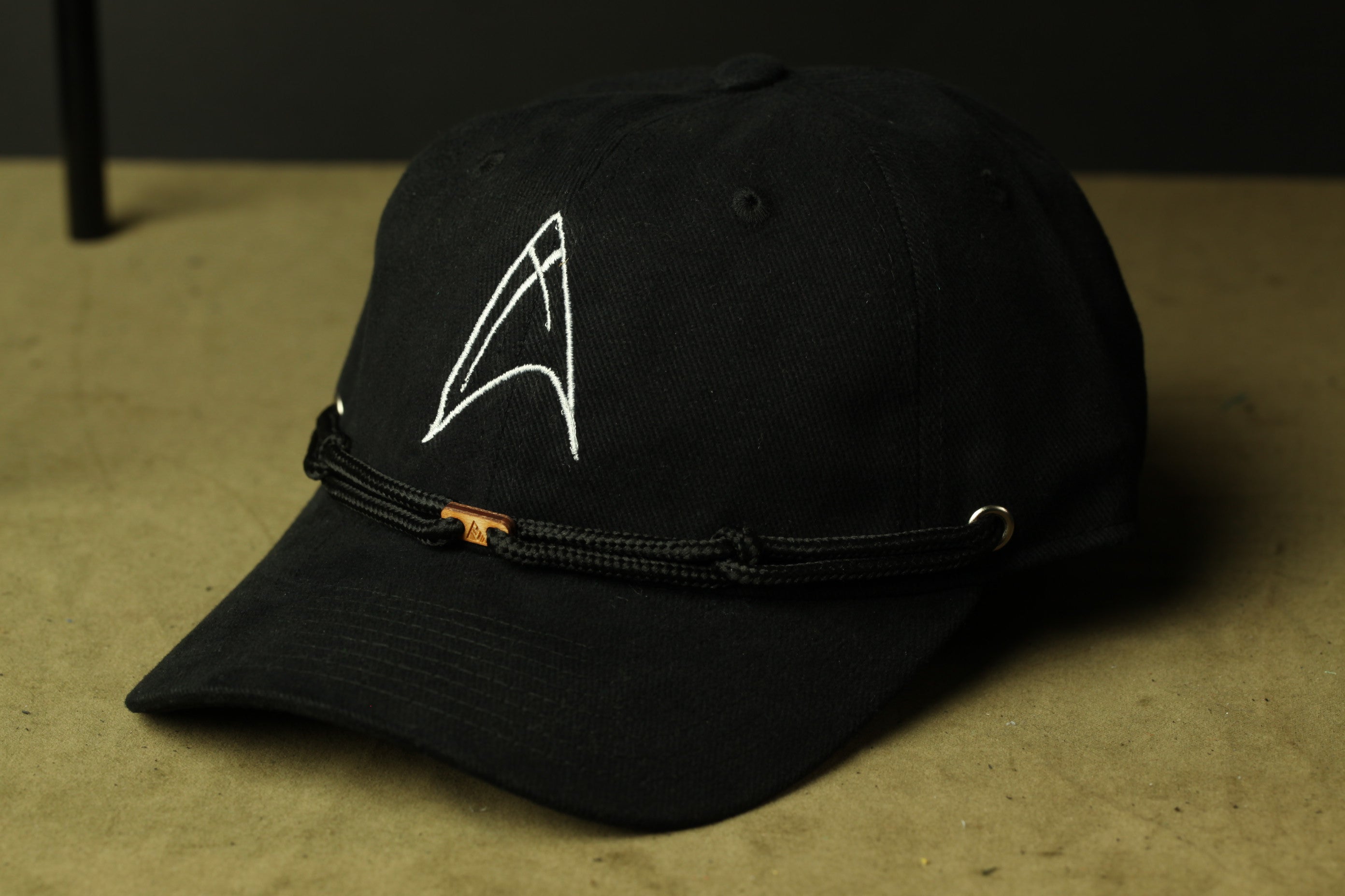 A black baseball cap with a white logo on the front, resting on a surface.