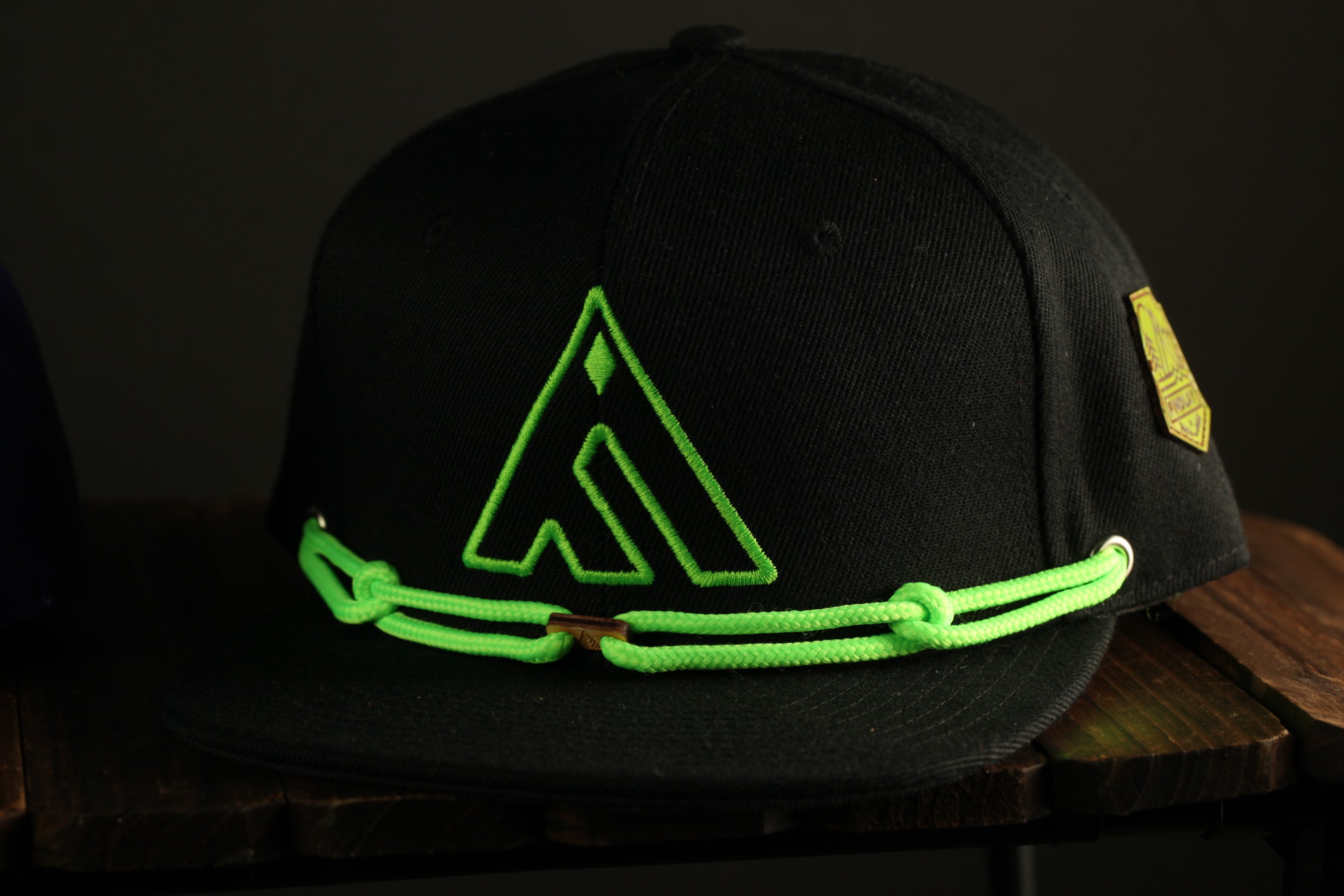 A black baseball cap with a green logo on it, sitting on a wooden surface.