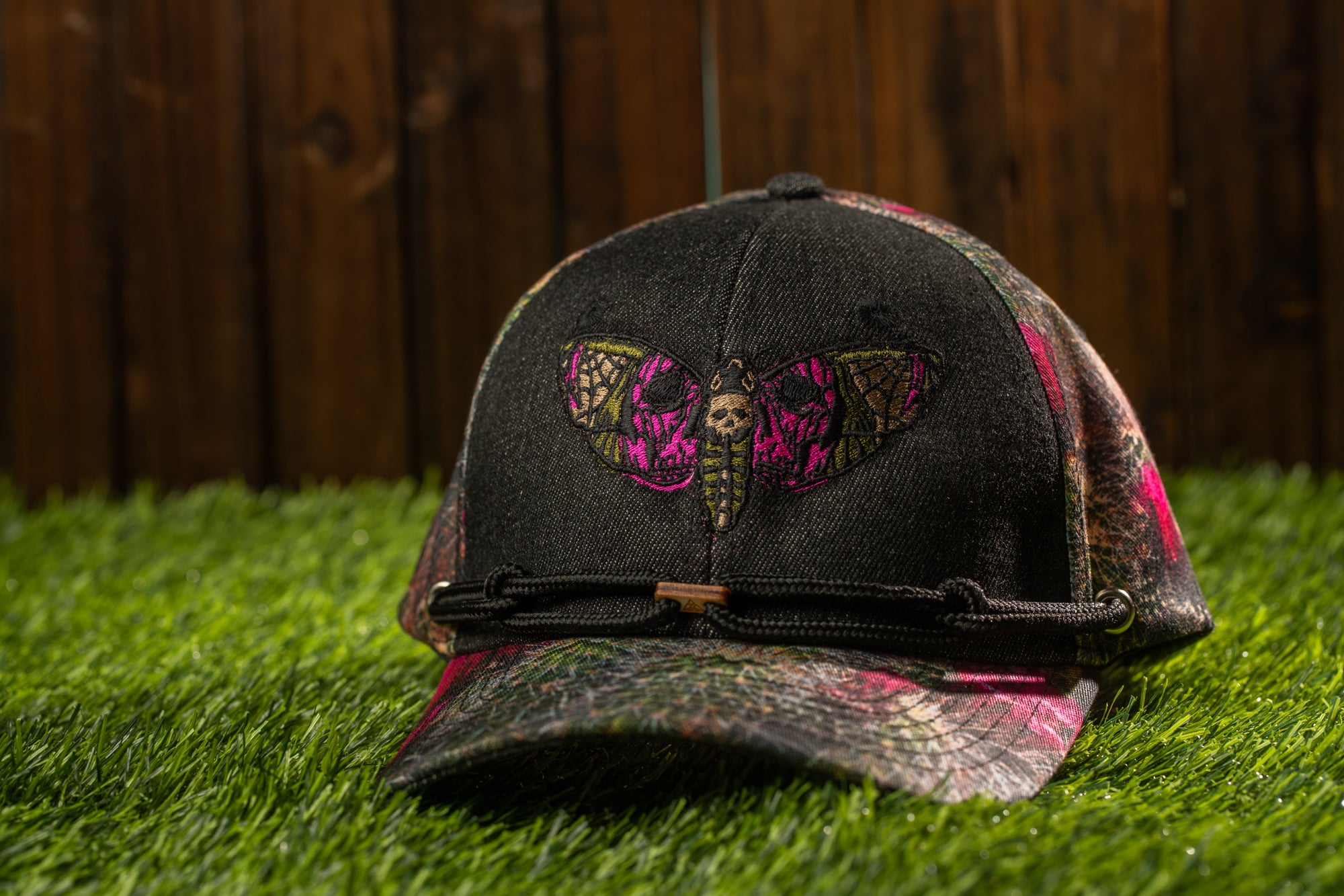 A black baseball cap with a colorful butterfly design on the front, resting on a grassy surface.