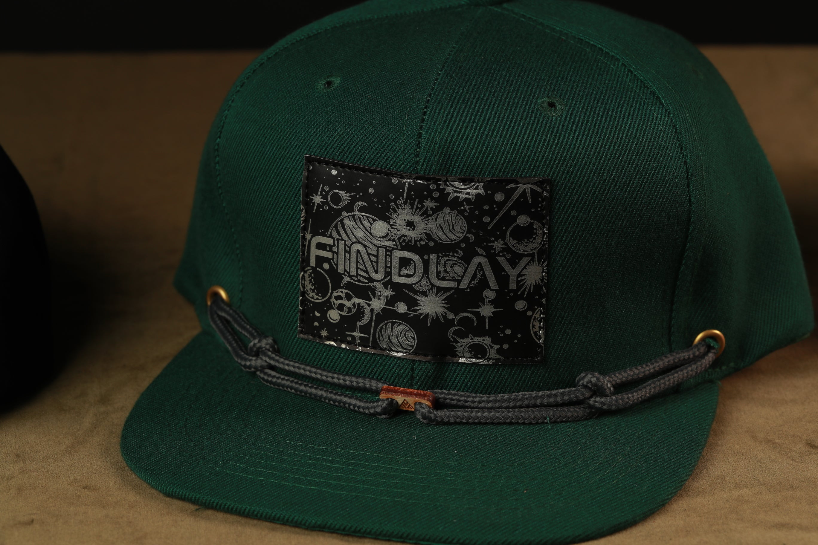 A green baseball cap with a black patch on the front displaying the word "FINDlay".
