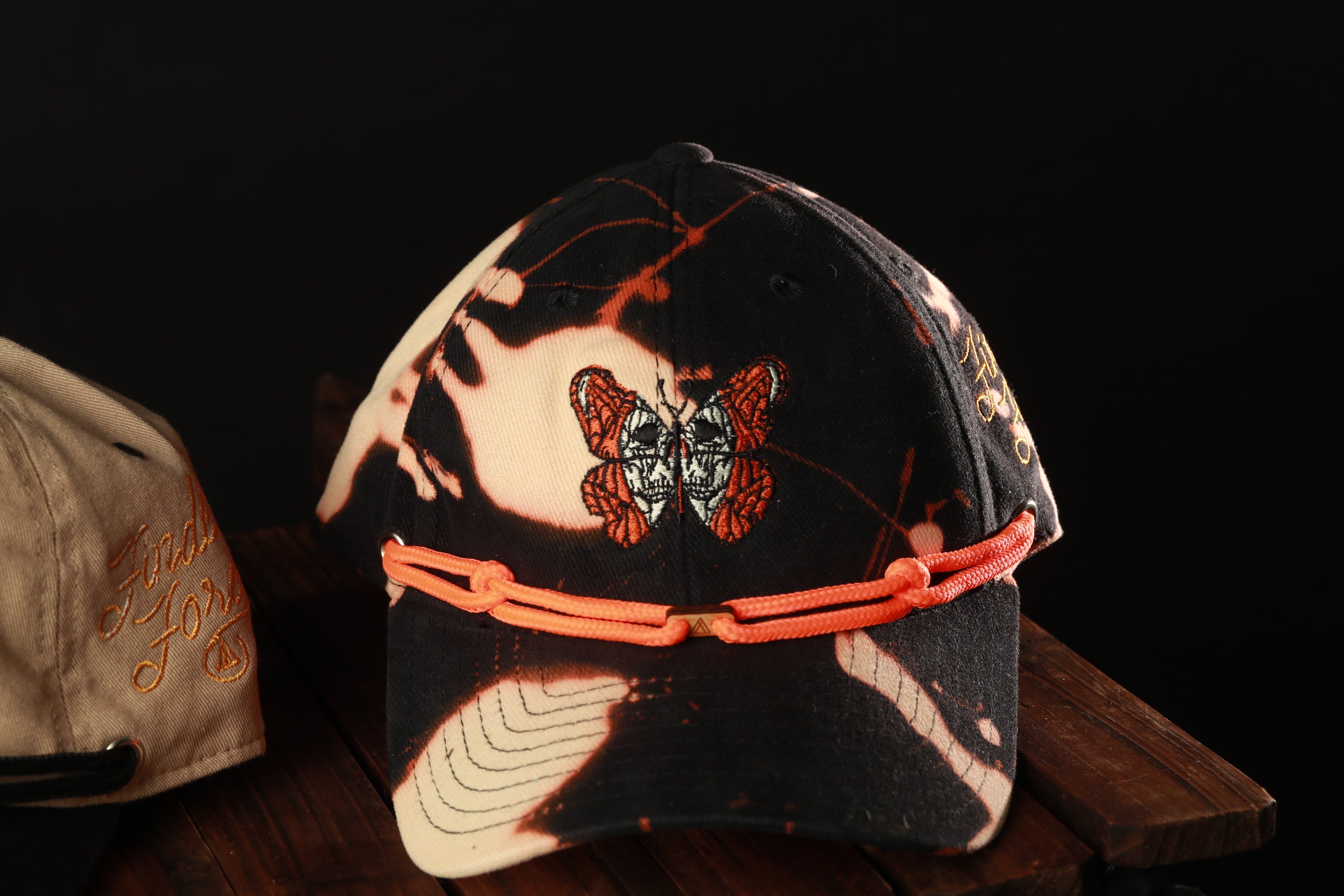 A black and orange patterned baseball cap with a butterfly design, resting on a wooden surface.