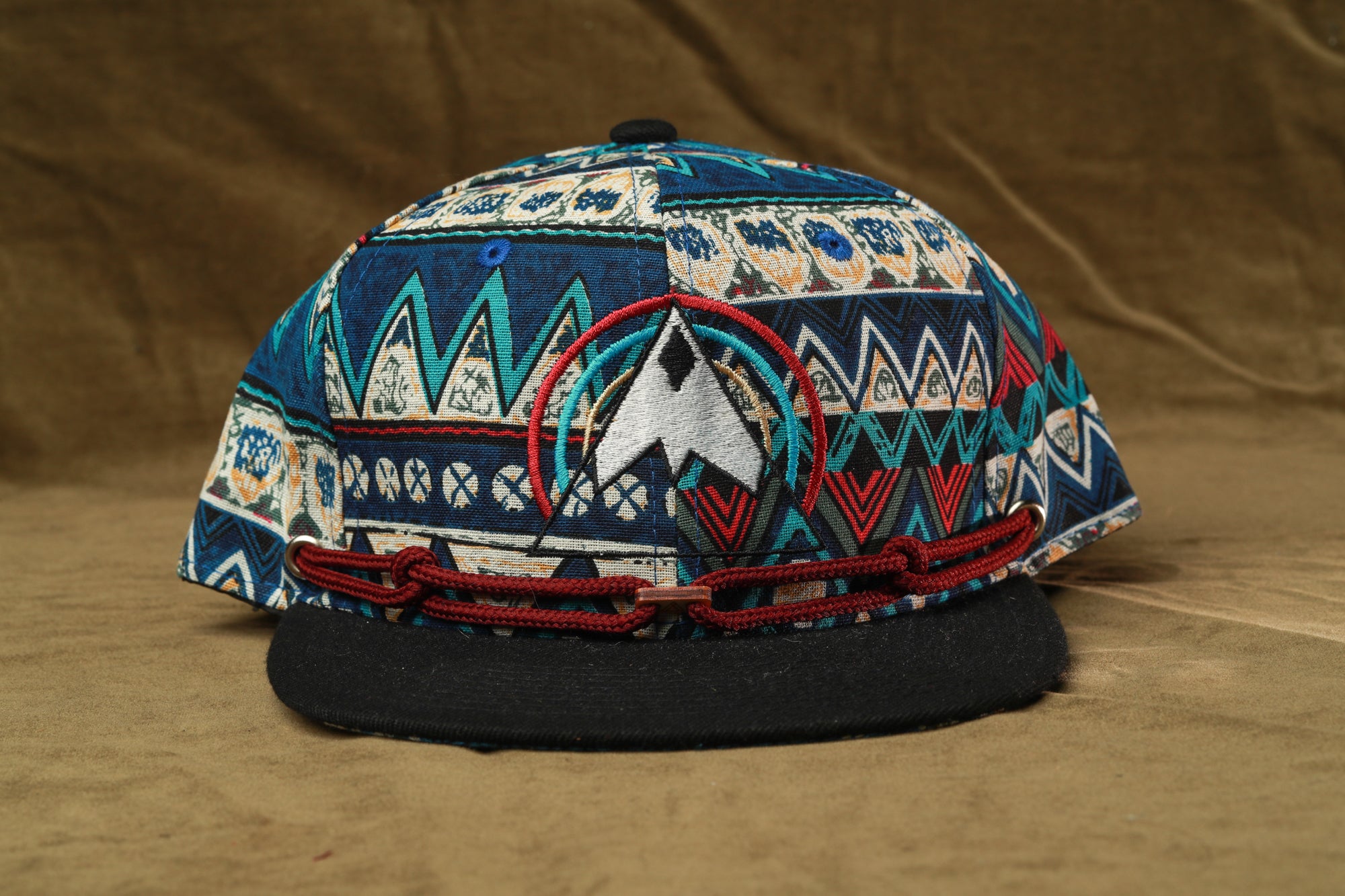 A colorful, patterned baseball cap with a black brim and a red chain strap.