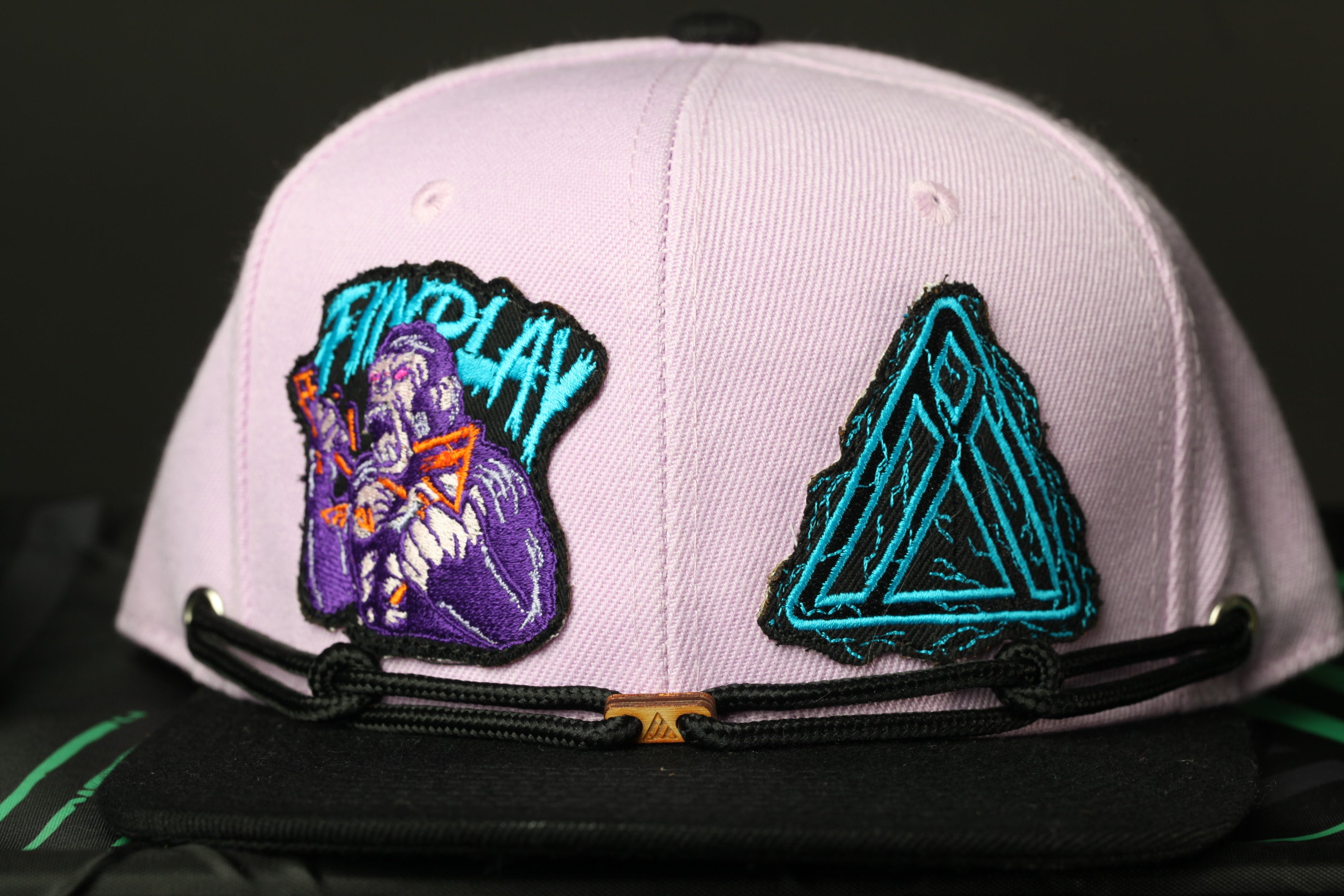 A pink baseball cap with two patches on it, one depicting a purple character and the other a triangular design.