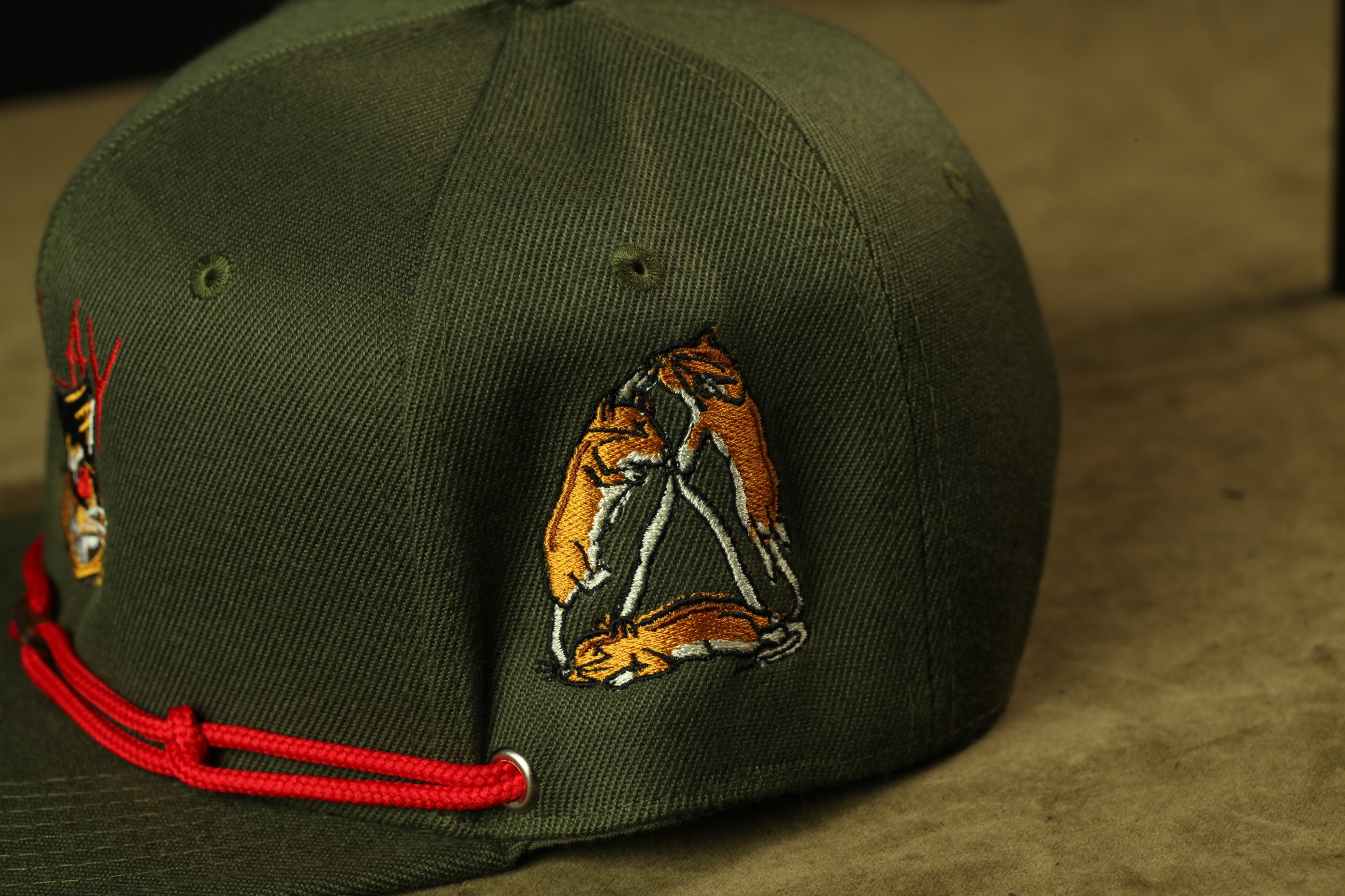 A close-up view of a green baseball cap with a red string and an embroidered design on the side.