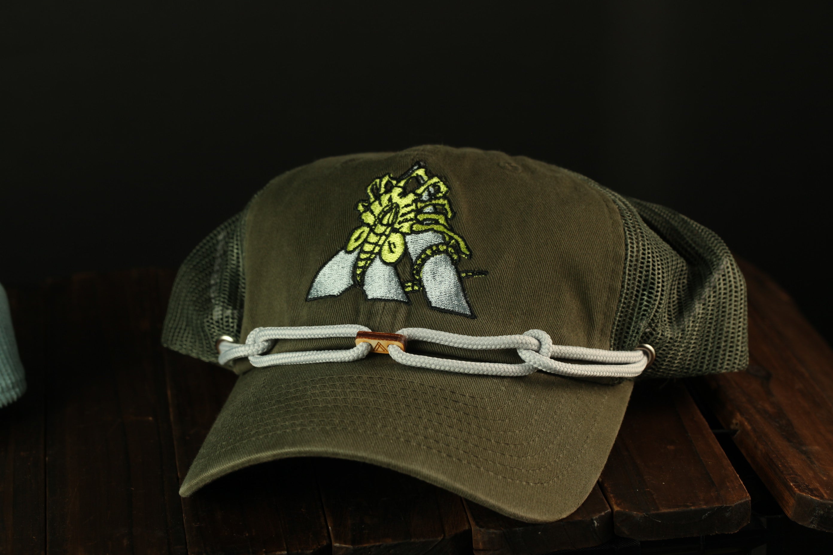 A green baseball cap with a yellow and black insect design on the front, resting on a wooden surface.