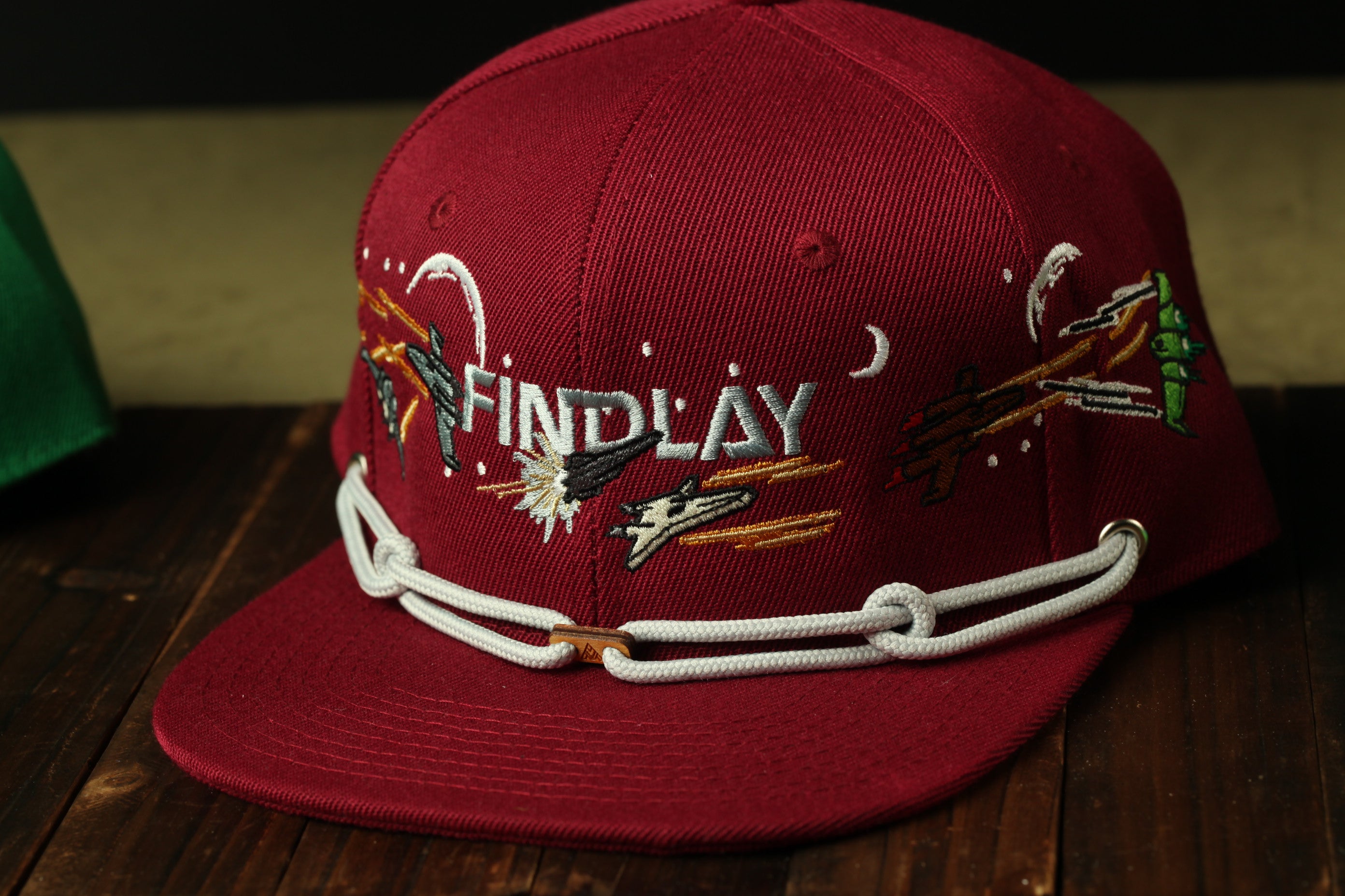 A red baseball cap with the word "FINDlay" embroidered on it, sitting on a wooden surface.