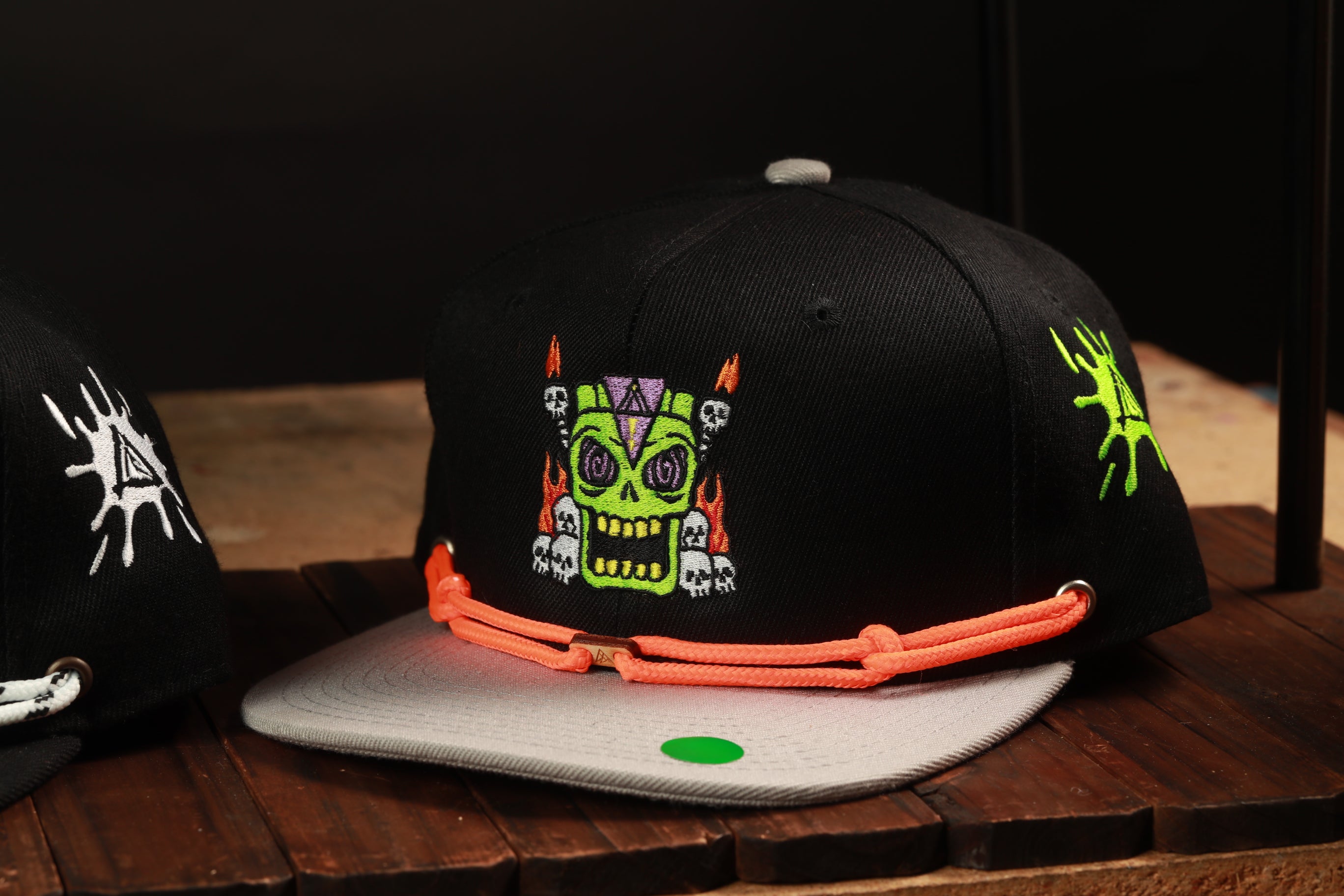 A black baseball cap with a colorful skull design and a red string is displayed on a wooden surface.
