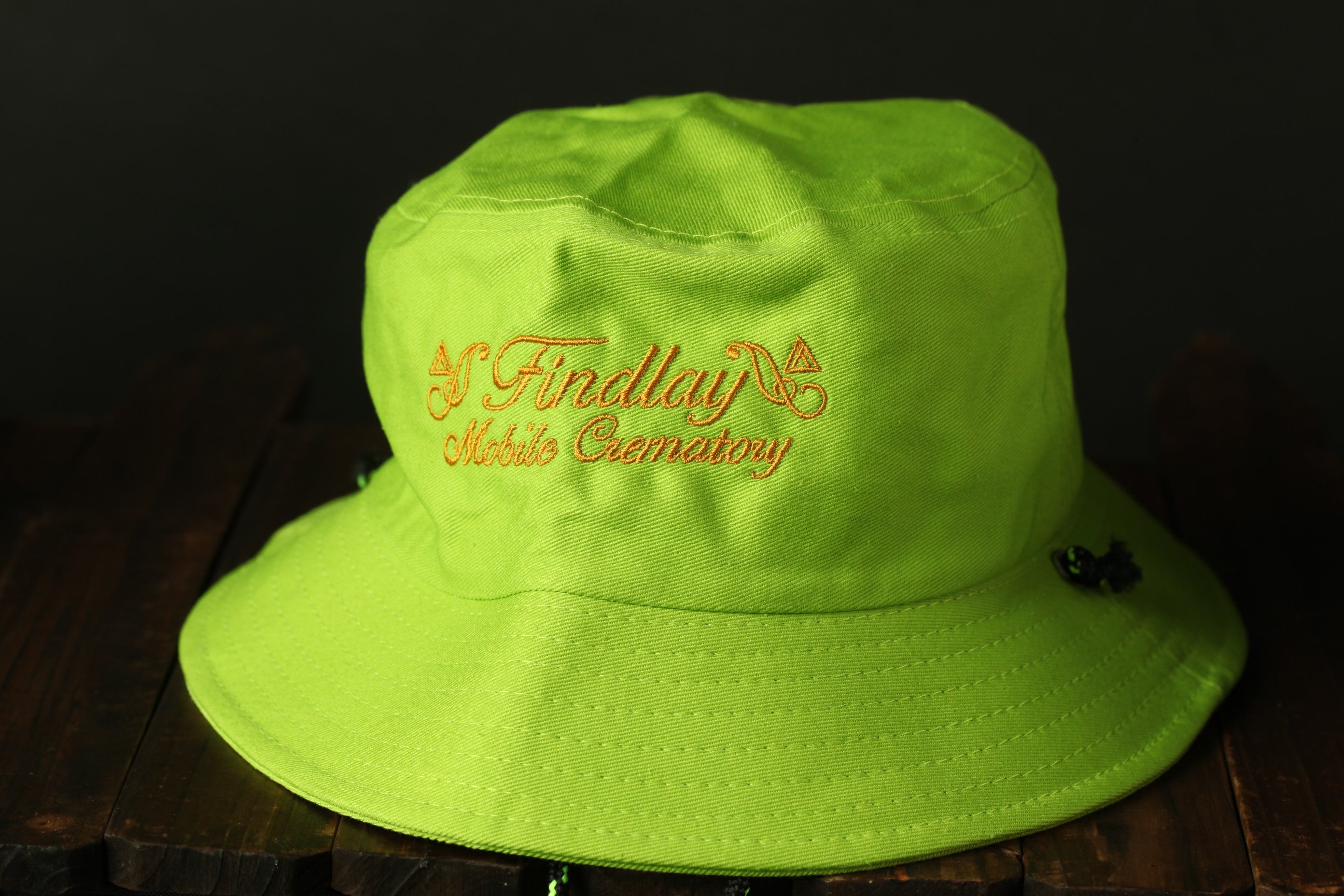 A bright green bucket hat with the text "Findlay Cemetery" embroidered on it.
