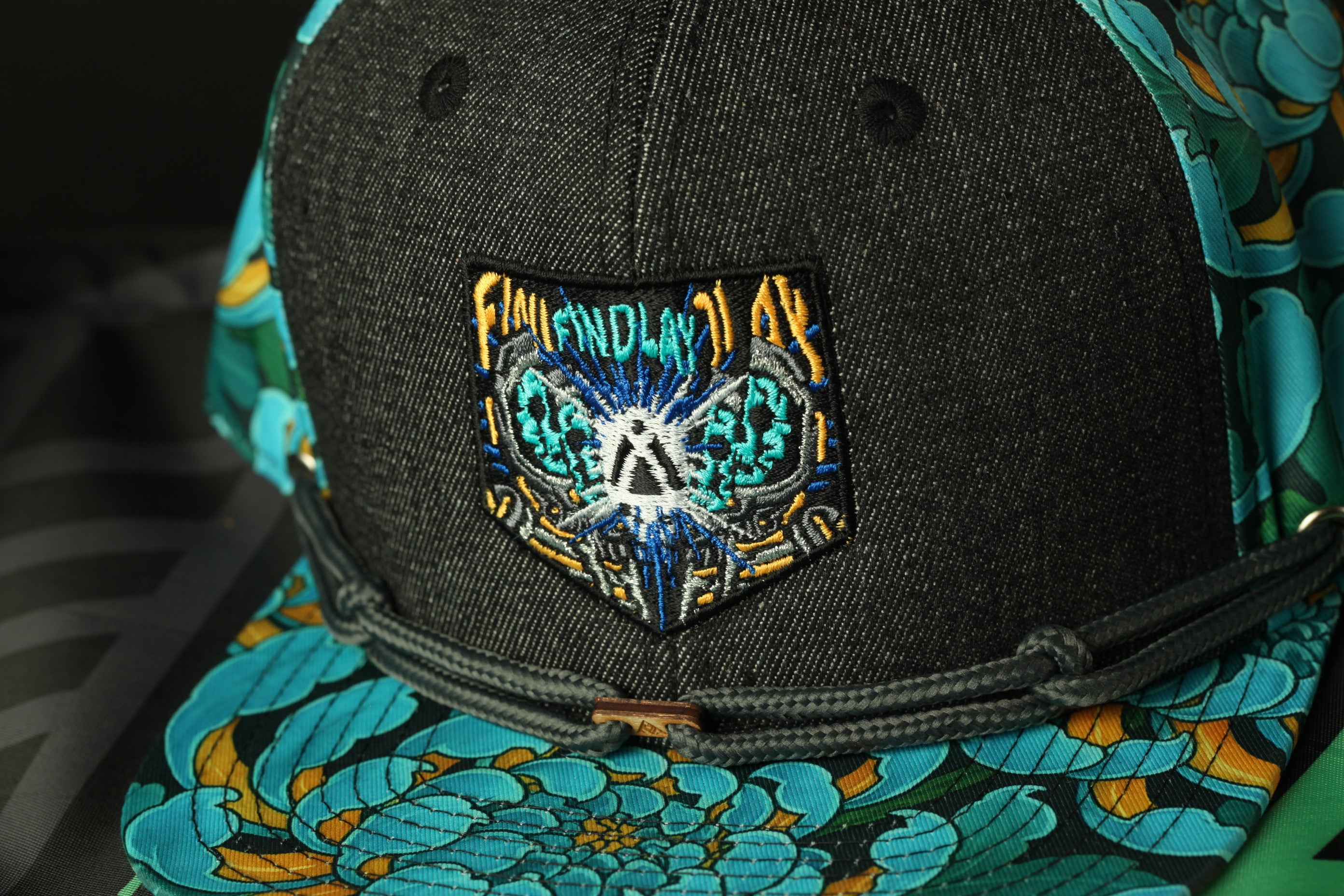 A close-up view of a black baseball cap with a colorful floral pattern and a patch on the front.