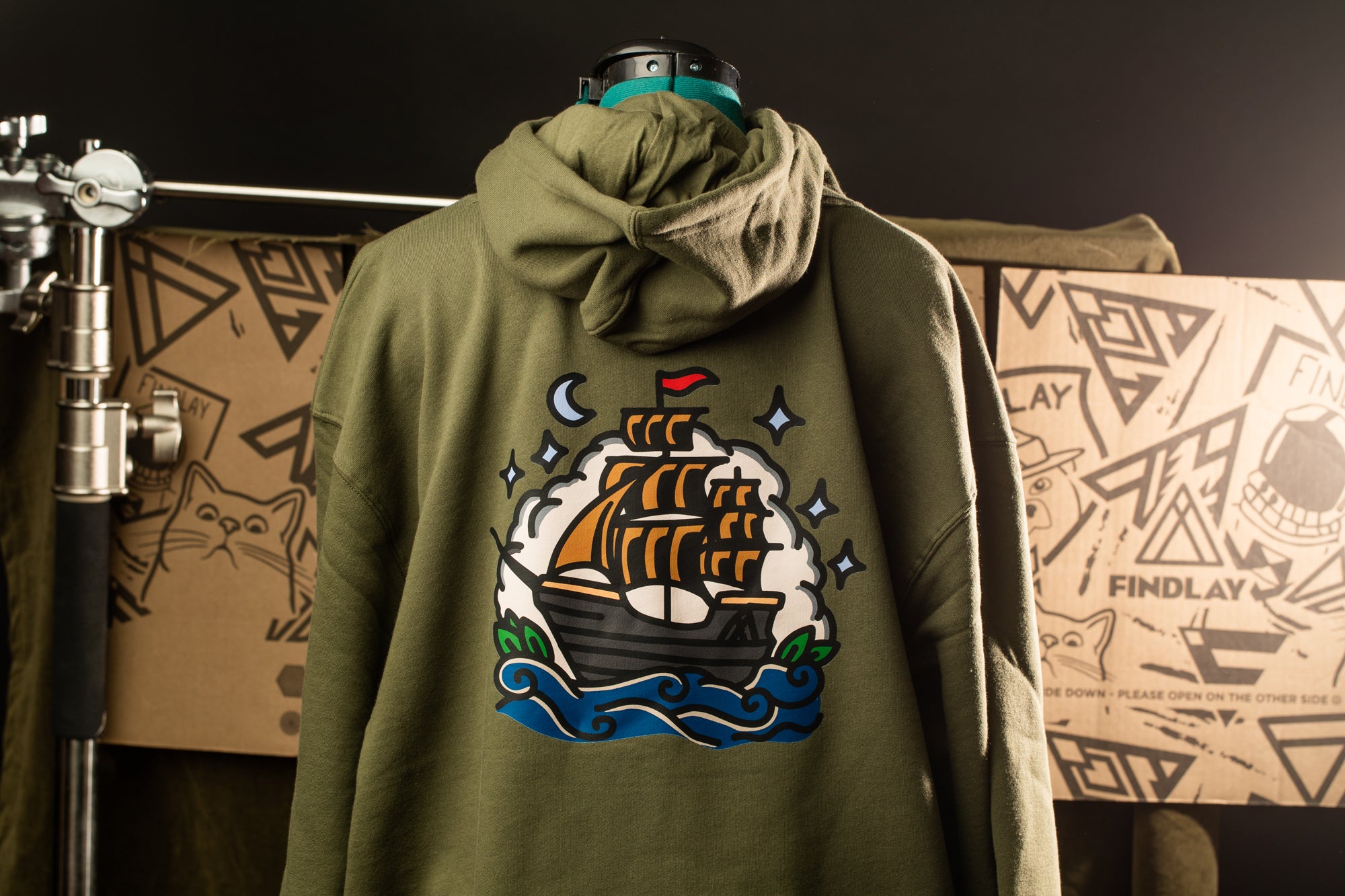 A mannequin wearing a green hoodie with a colorful graphic of a ship on the back.
