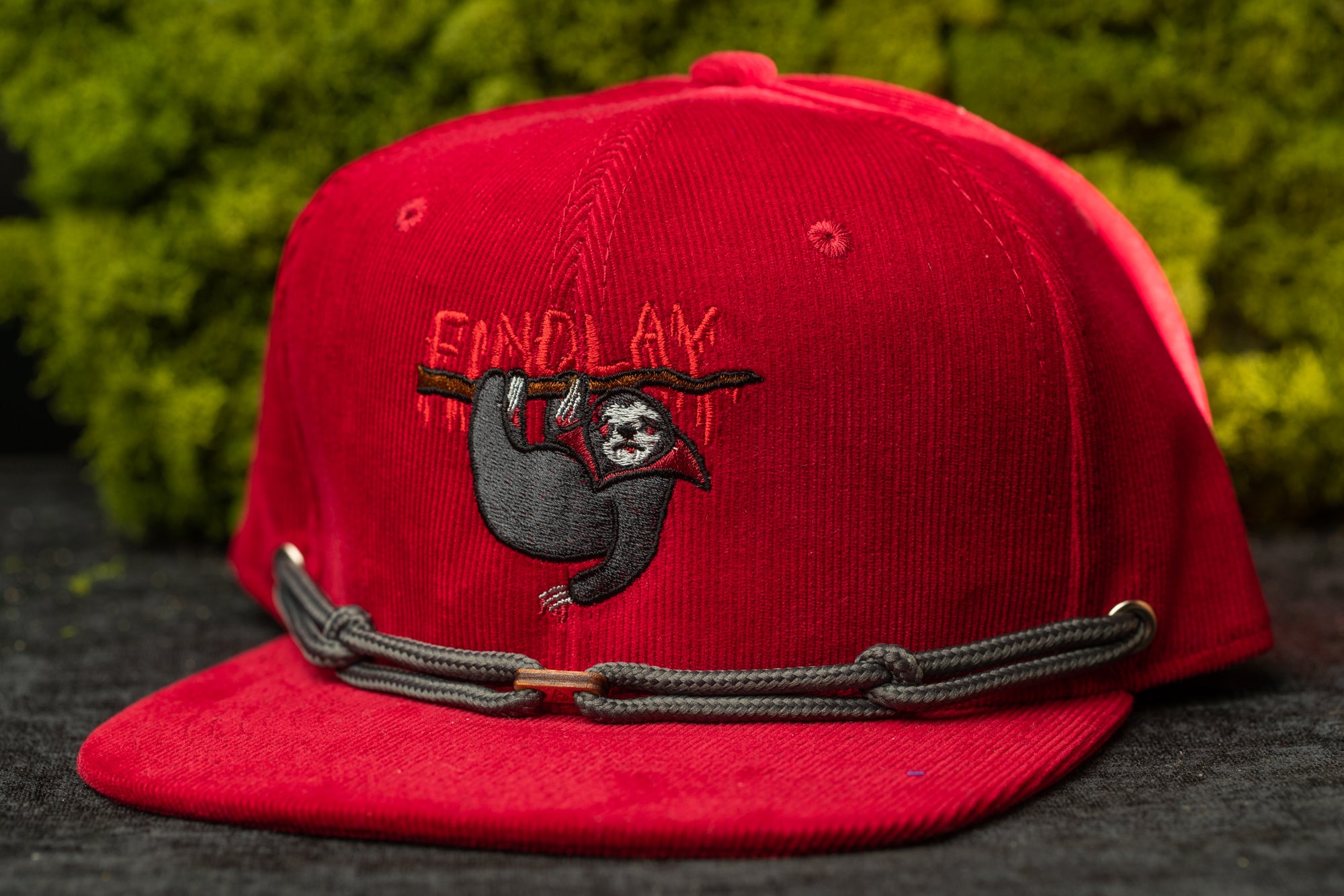 A red baseball cap with a sloth graphic and the word "FIND LAY" printed on it.