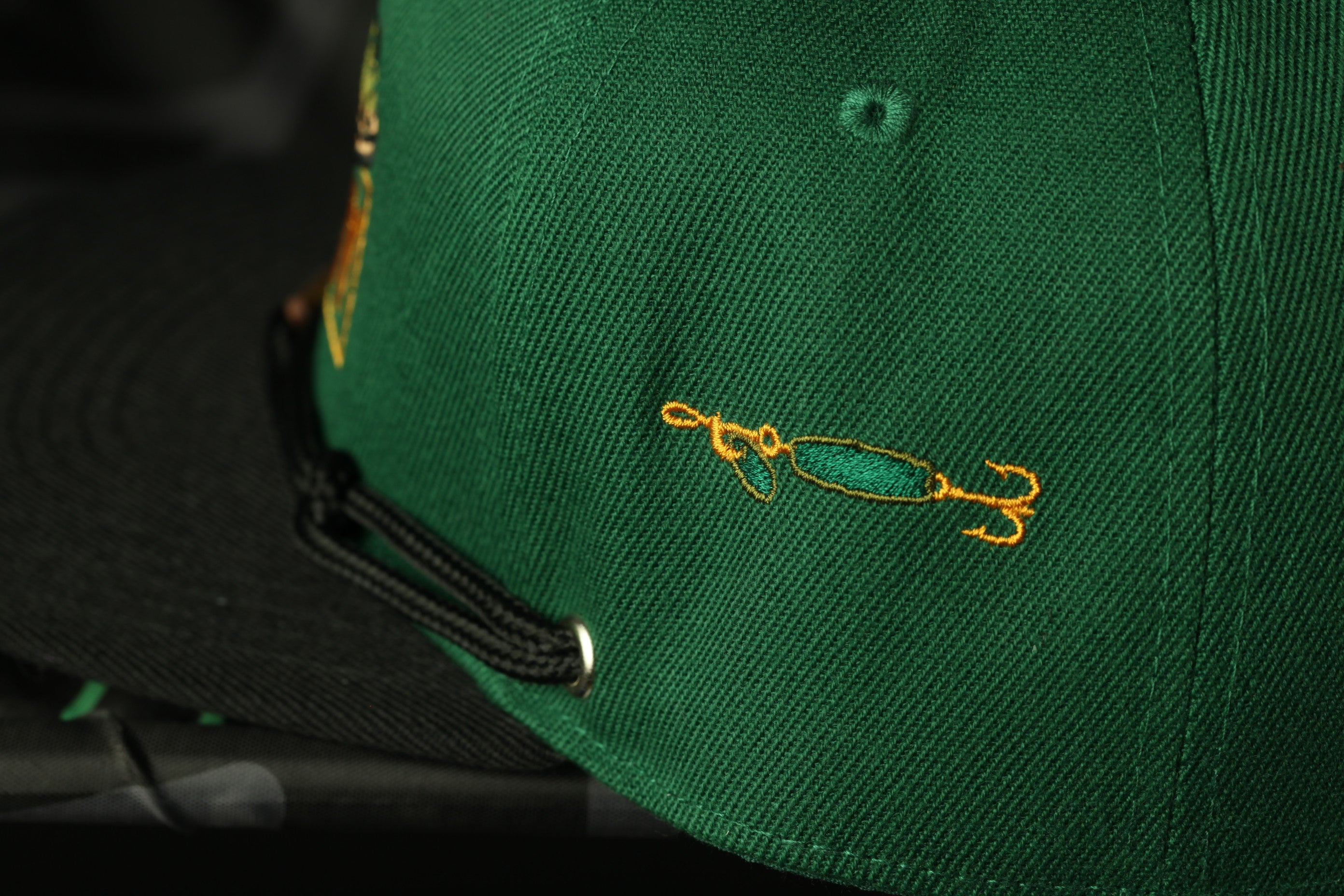 A close-up view of a green baseball cap with a fishing-themed embroidered design on the front.