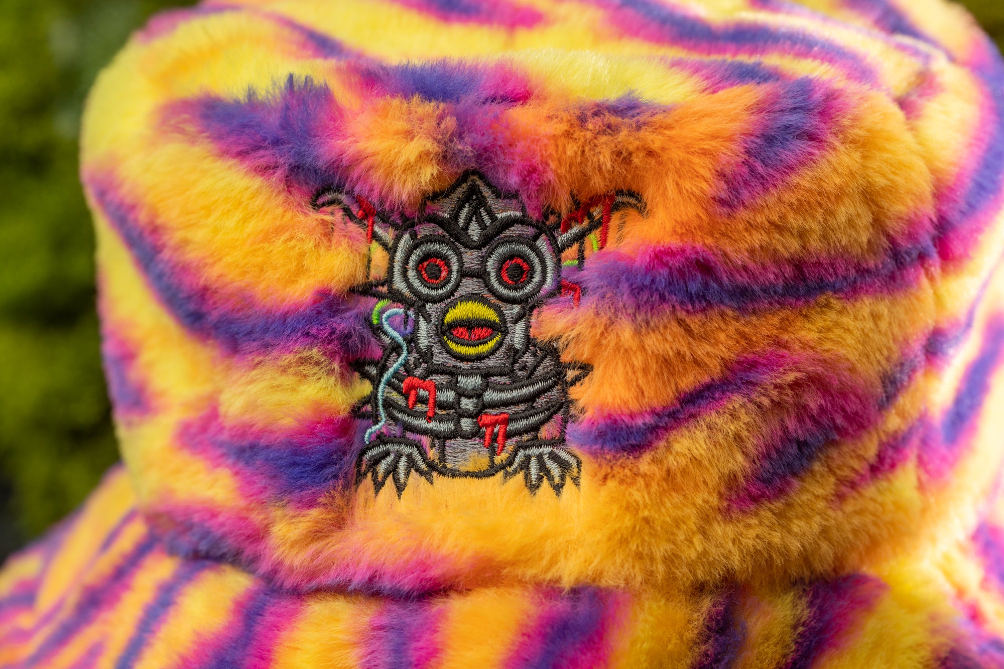 A close-up of a colorful, fuzzy hat with a unique, embroidered design featuring a stylized, cartoonish creature.