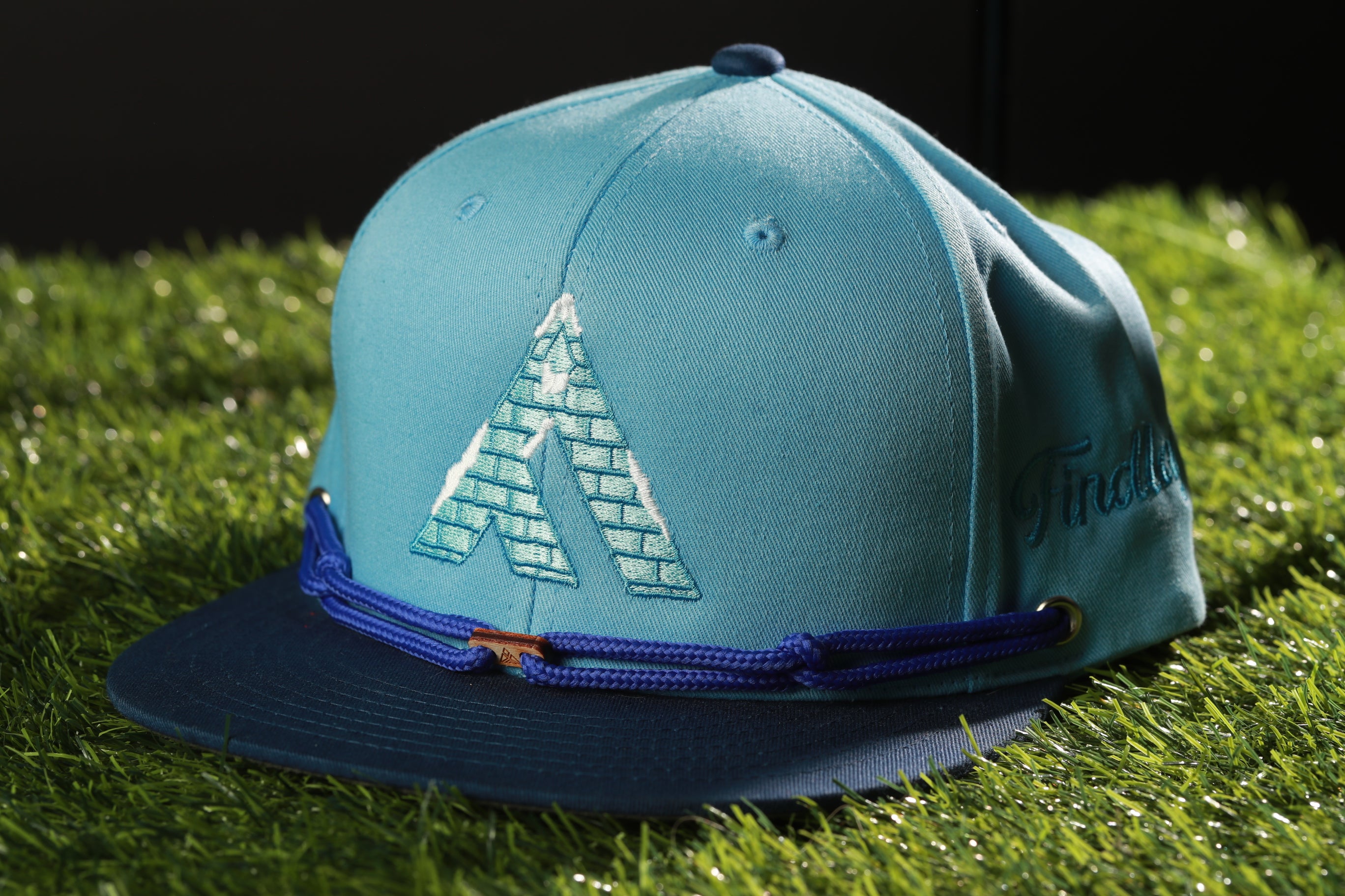 A blue baseball cap with a brick pattern on the front, placed on a grassy surface.