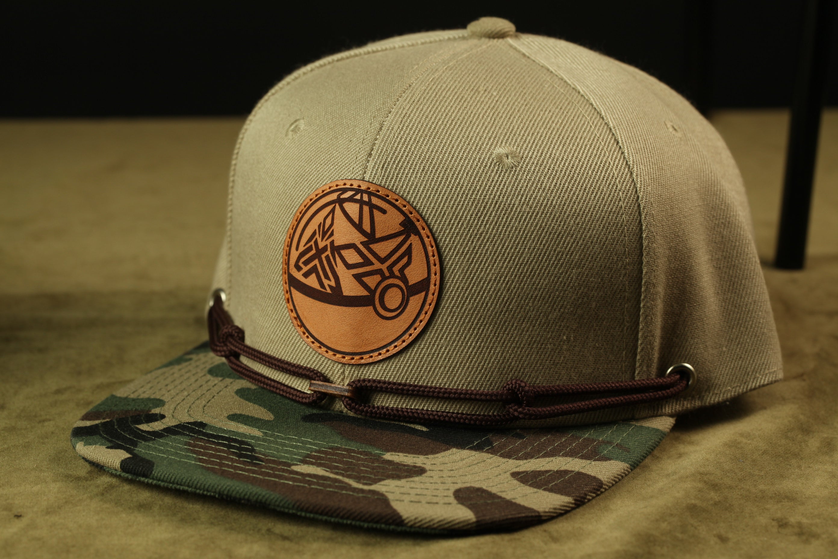 A beige baseball cap with a camouflage pattern and a circular patch on the front.