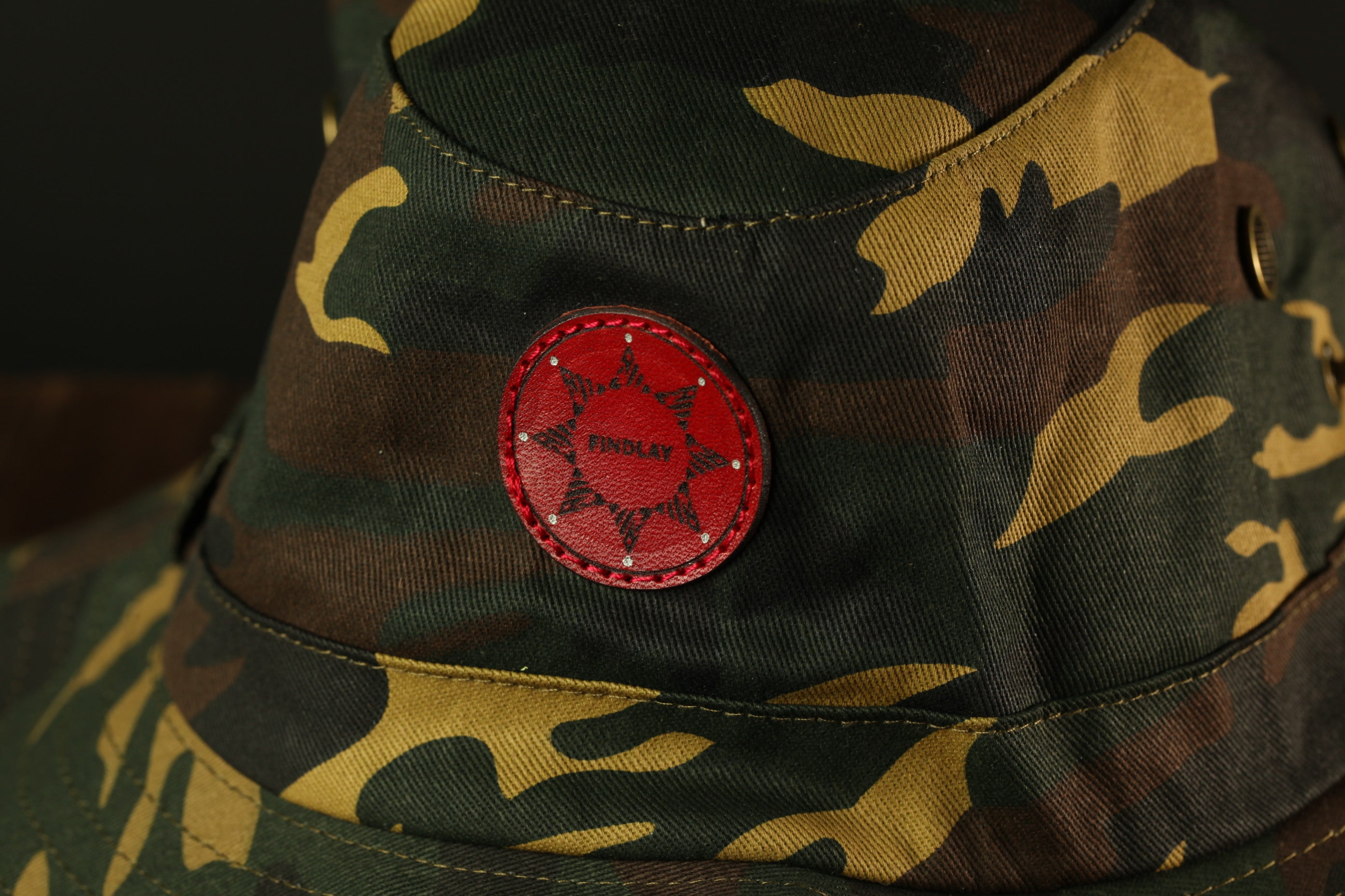 A close-up view of a camouflage military hat with a red star-shaped patch on the front.