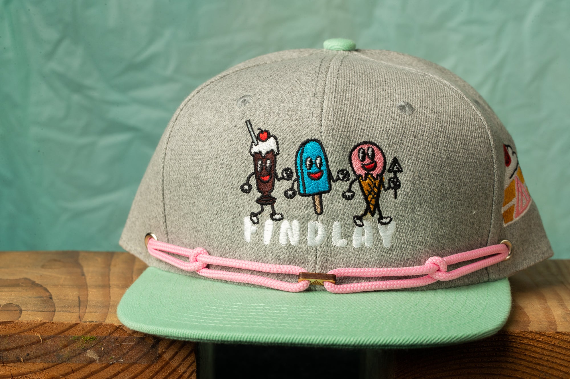 A gray baseball cap with a cartoon ice cream character design and the word "FINDPLAY" printed on it.