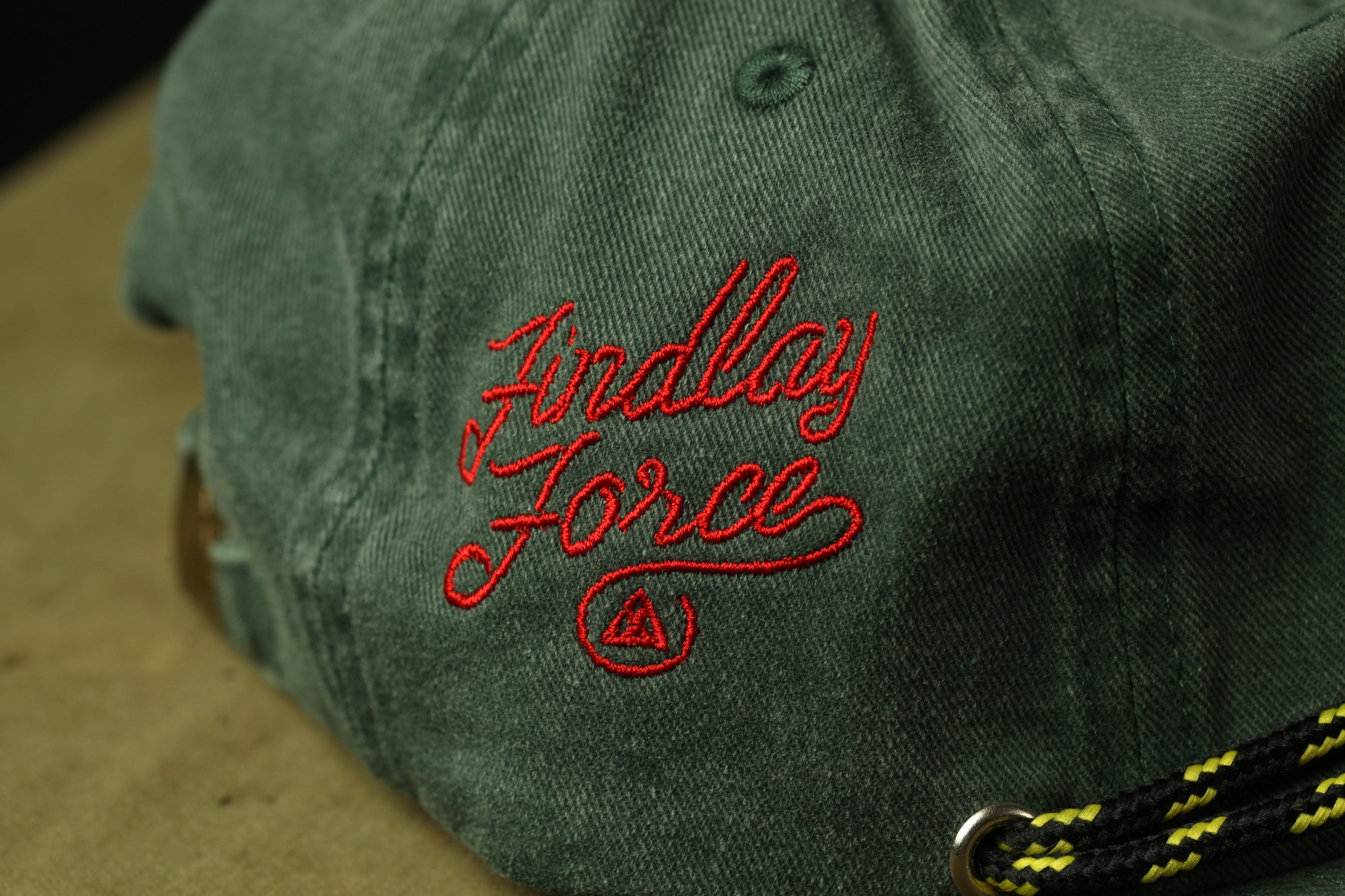 A close-up view of a green baseball cap with red embroidered text on it.
