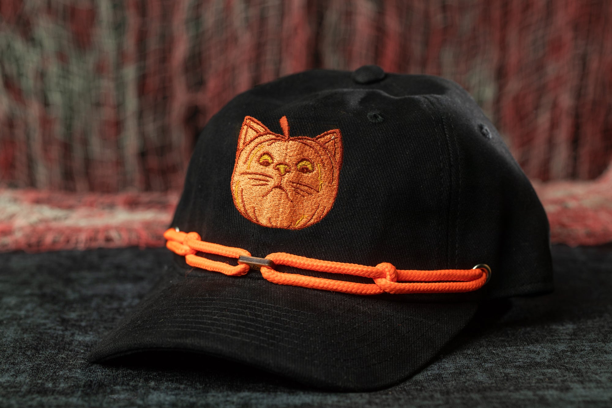 A black baseball cap with an orange cat embroidered on it, featuring a chain strap.