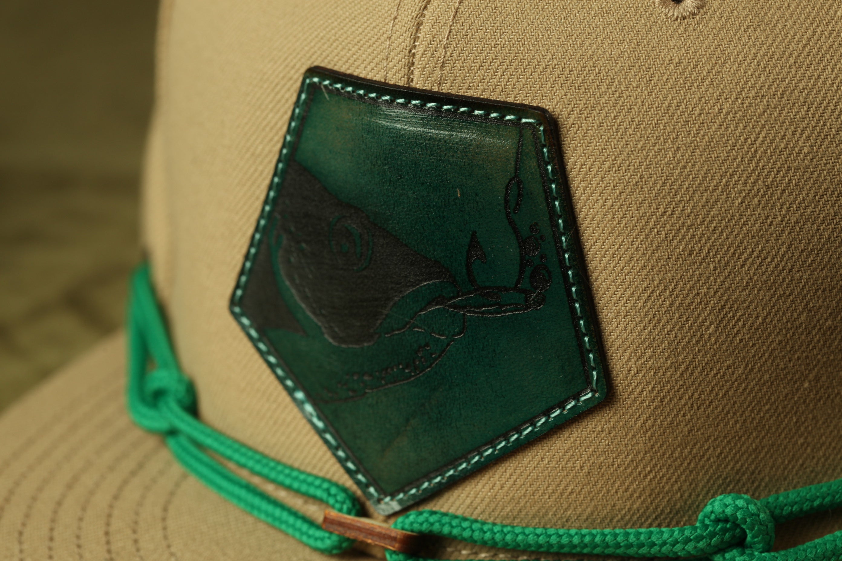 A close-up view of a beige baseball cap with a green and black embroidered patch on the front.