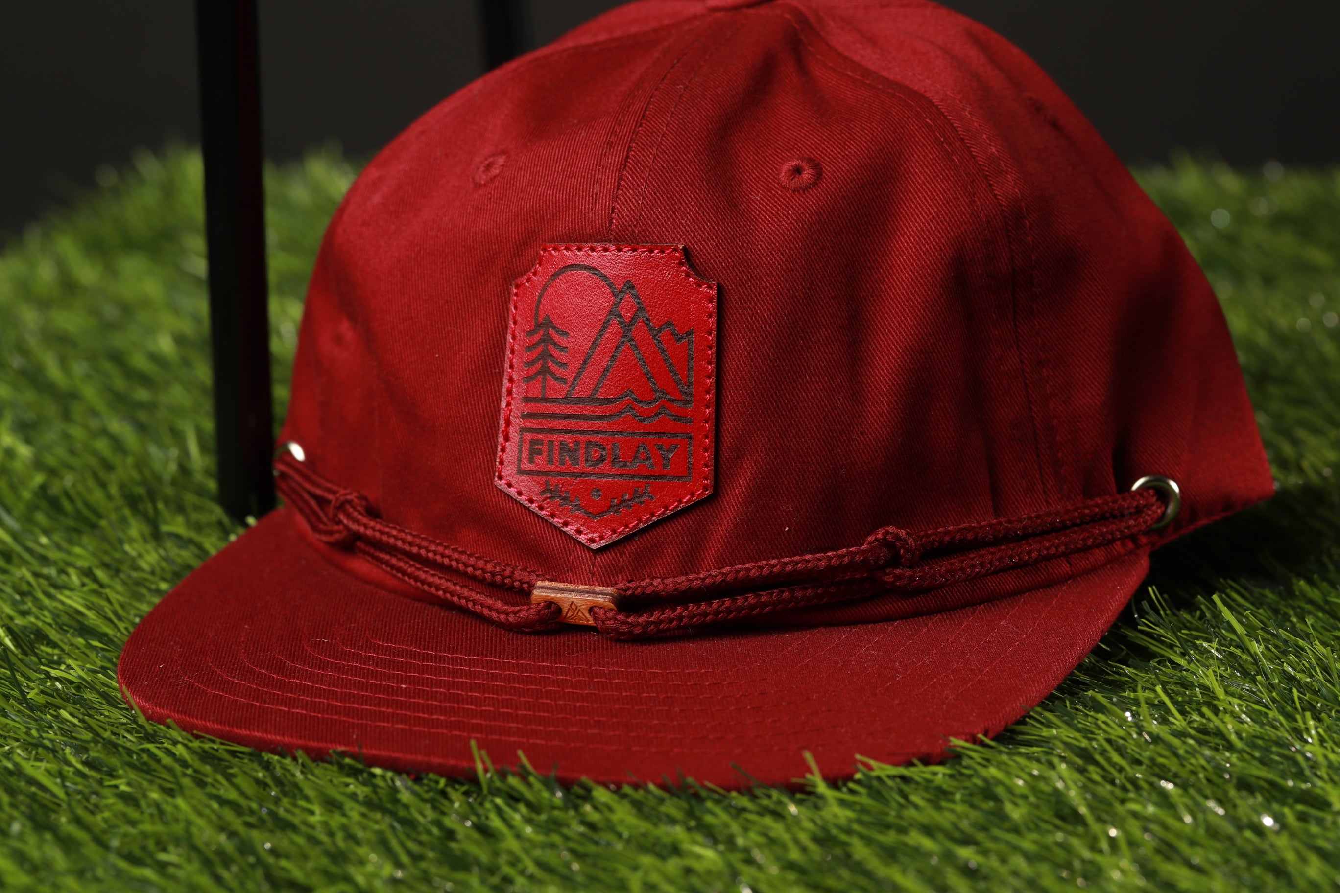 A red baseball cap with a red and black logo on the front, placed on a green surface.