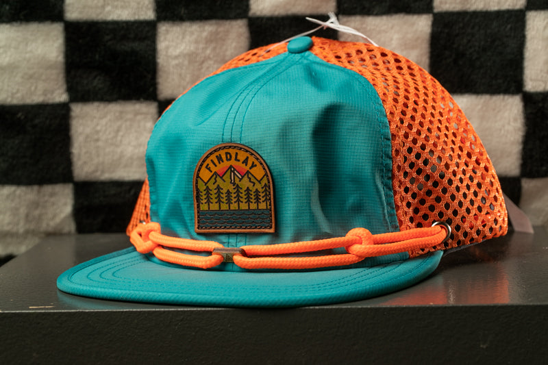 A turquoise baseball cap with an orange mesh panel and a patch on the front, sitting on a black surface against a checkered background.