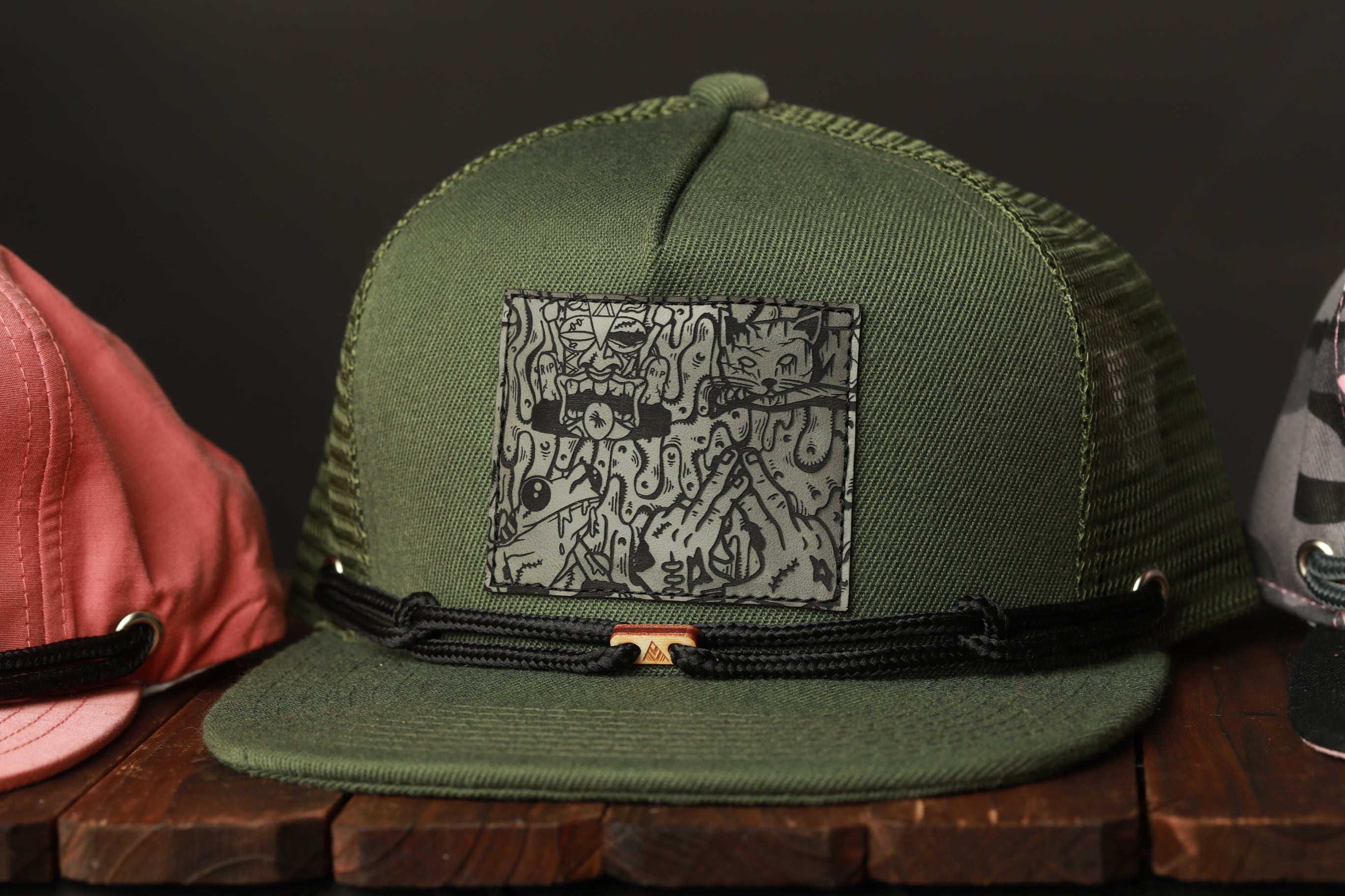 A green baseball cap with a graphic design on the front, sitting on a wooden surface.