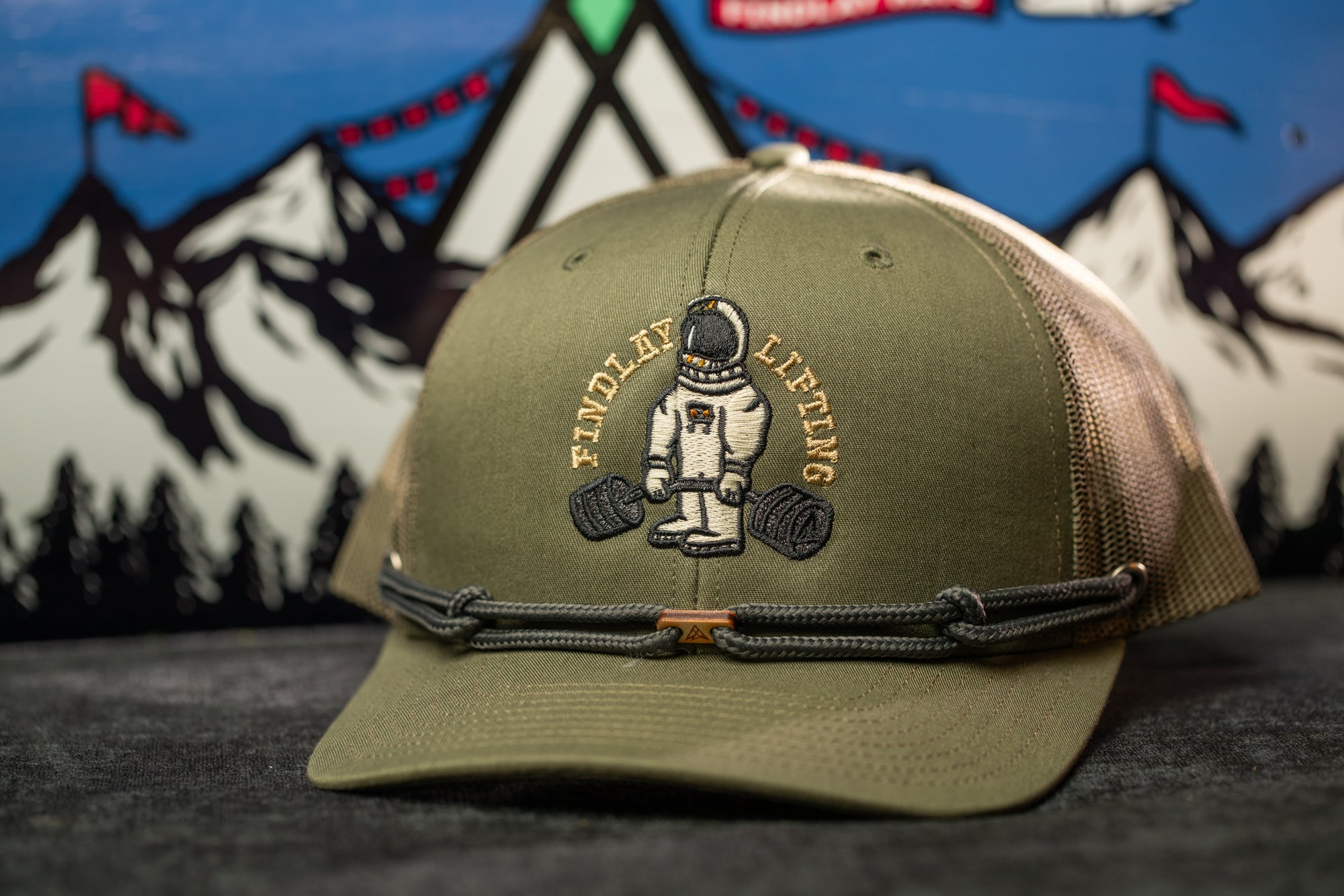 A green baseball cap with a graphic of a person lifting weights and the text "Findlay Lifting" on it, placed on a gray surface.
