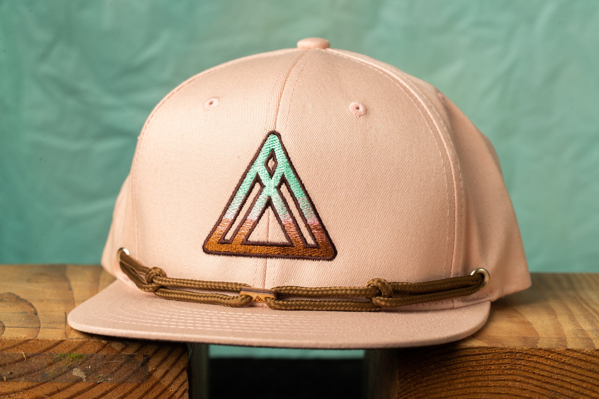 A pink baseball cap with a triangular embroidered logo on the front, sitting on a wooden surface.