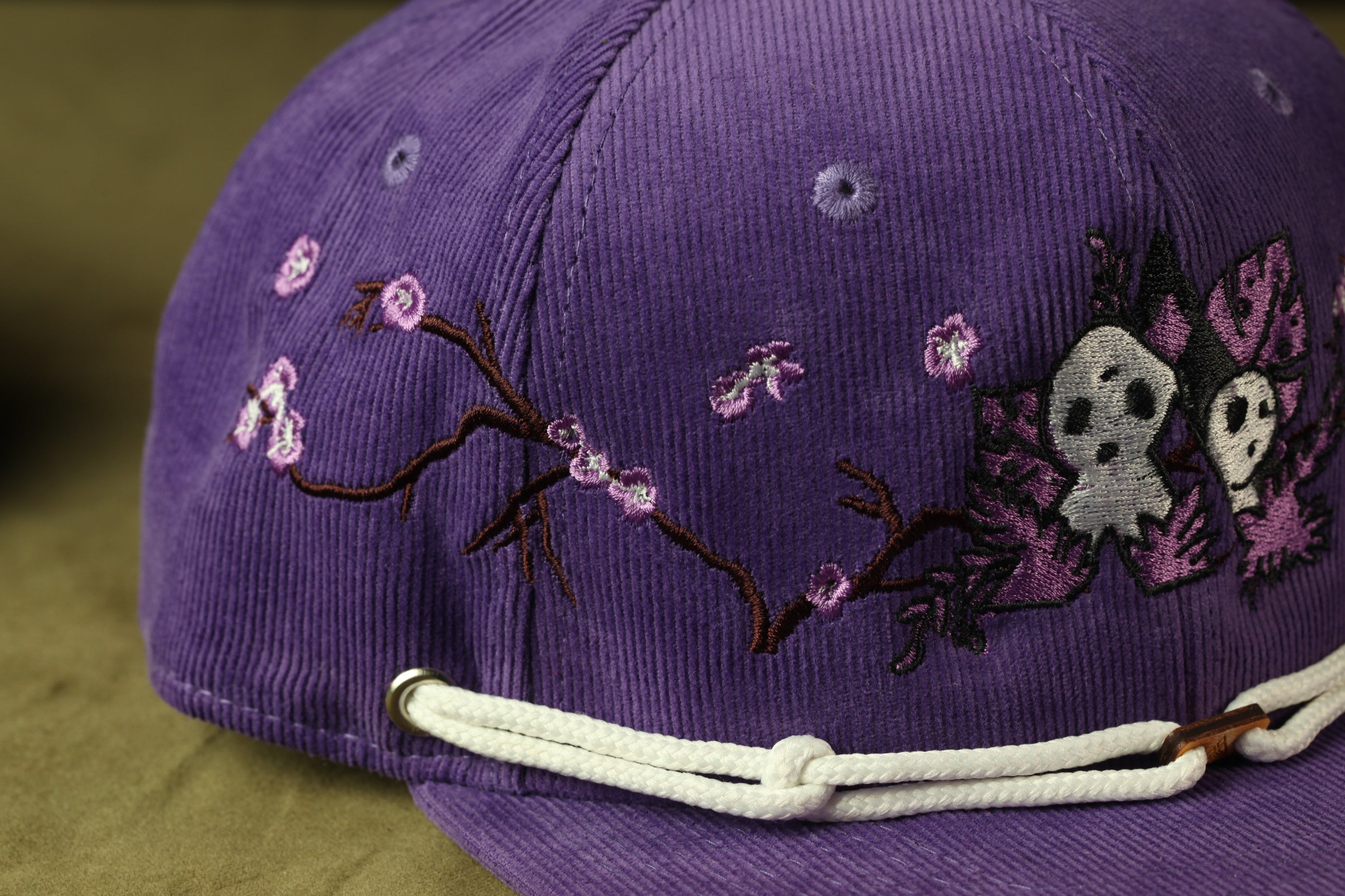 A close-up view of a purple baseball cap with floral embroidery and a white strap.