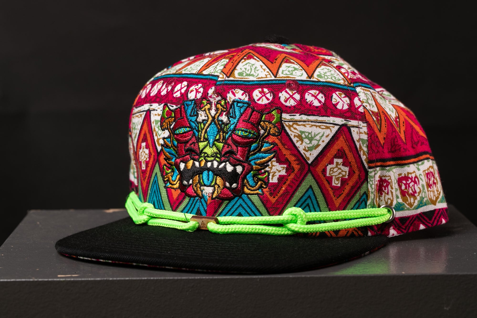 A colorful, patterned baseball cap with a dragon design on the front, featuring a mix of red, green, and yellow colors.