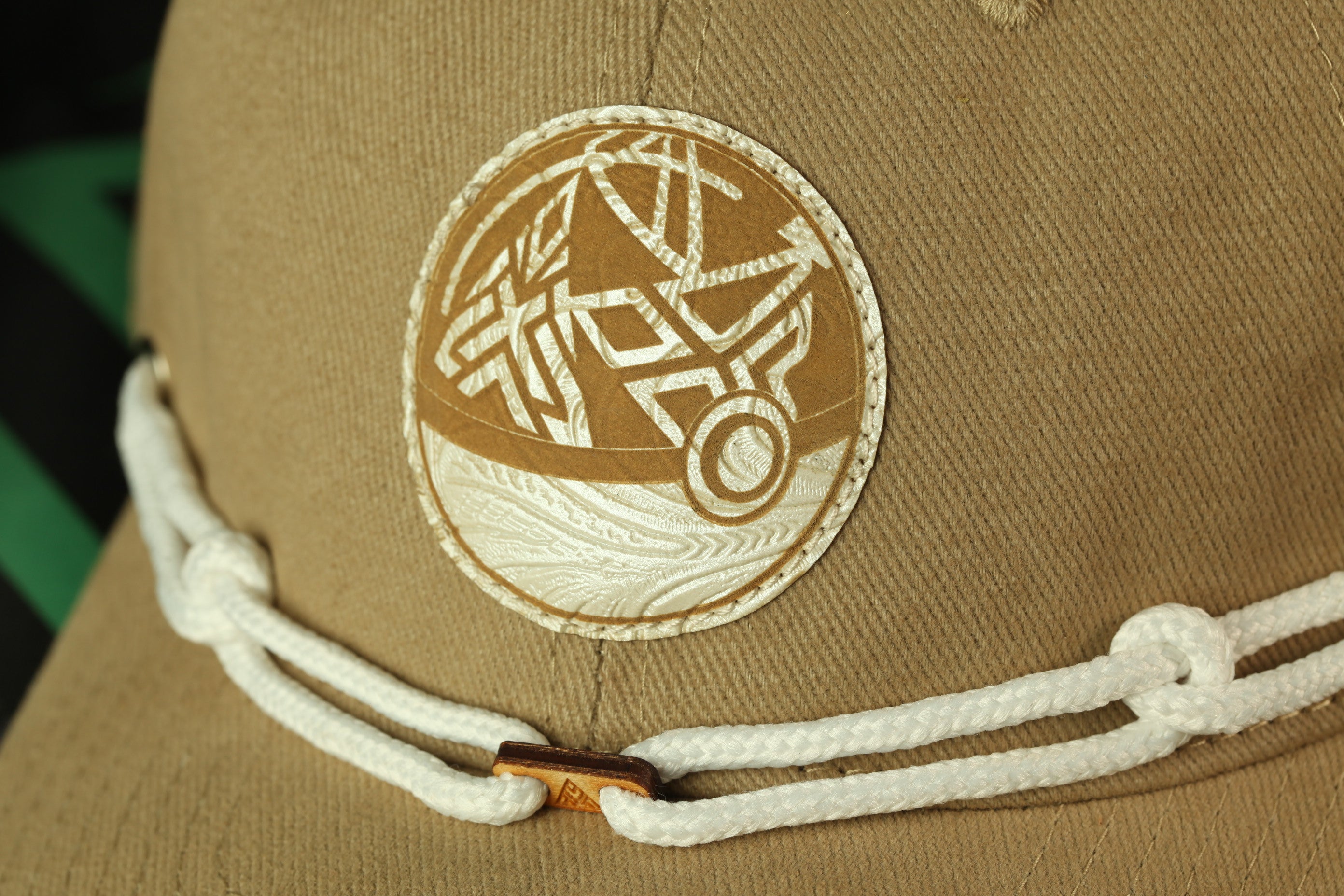 A close-up view of a beige hat with a decorative circular patch on the front.