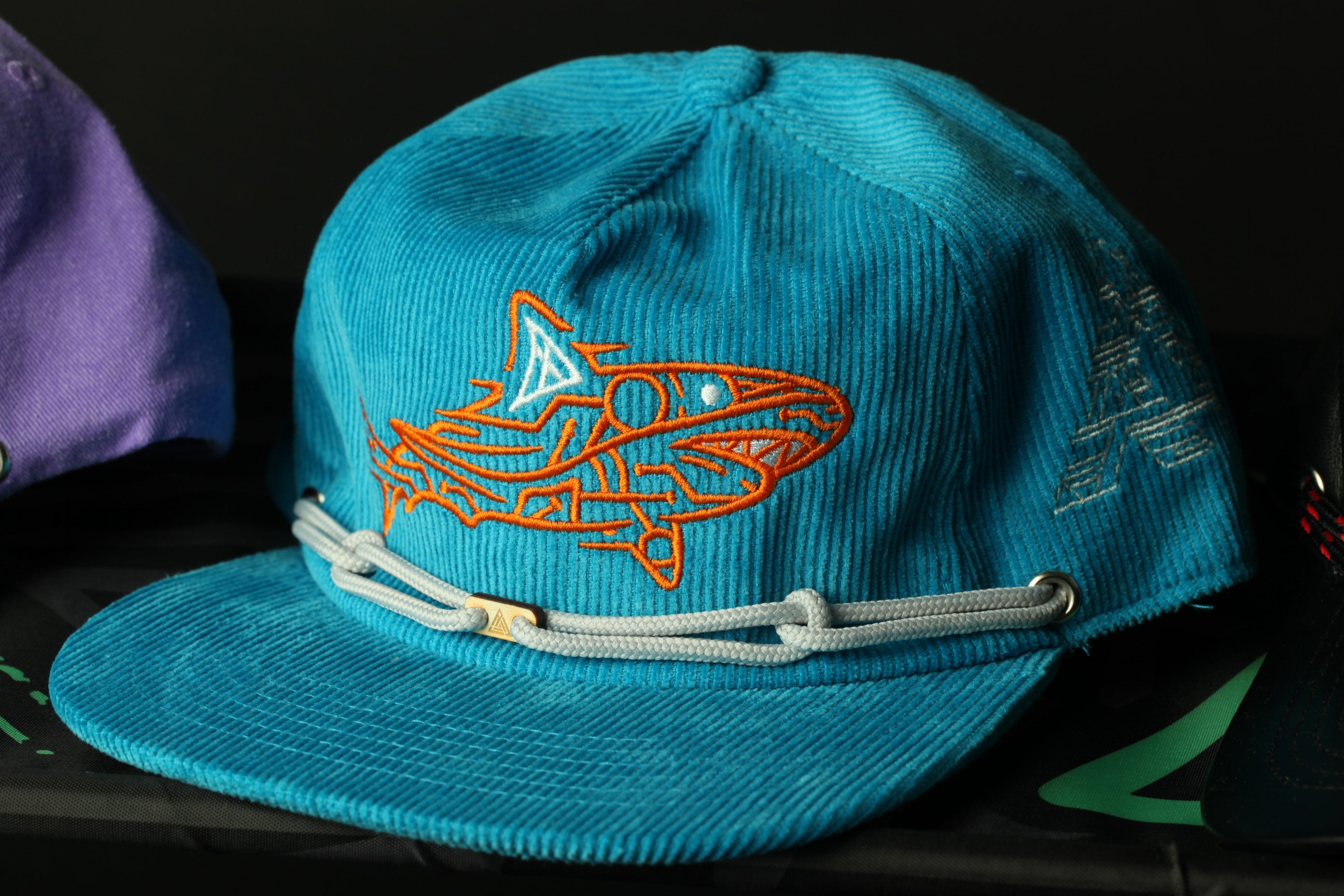 A blue baseball cap with an orange shark design on it.