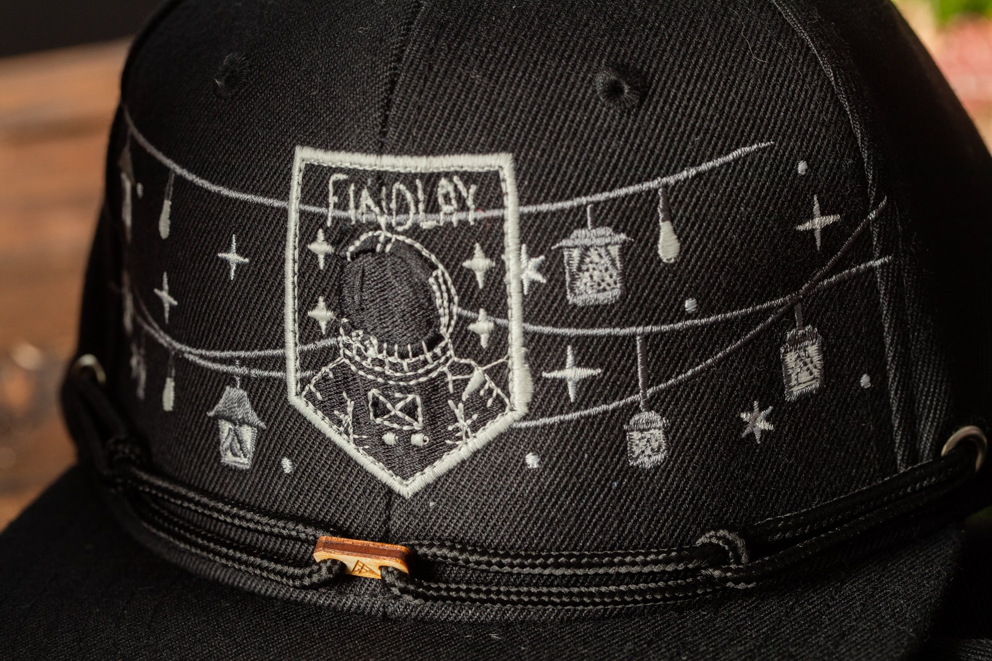A close-up view of a black baseball cap with a white embroidered design on the front.