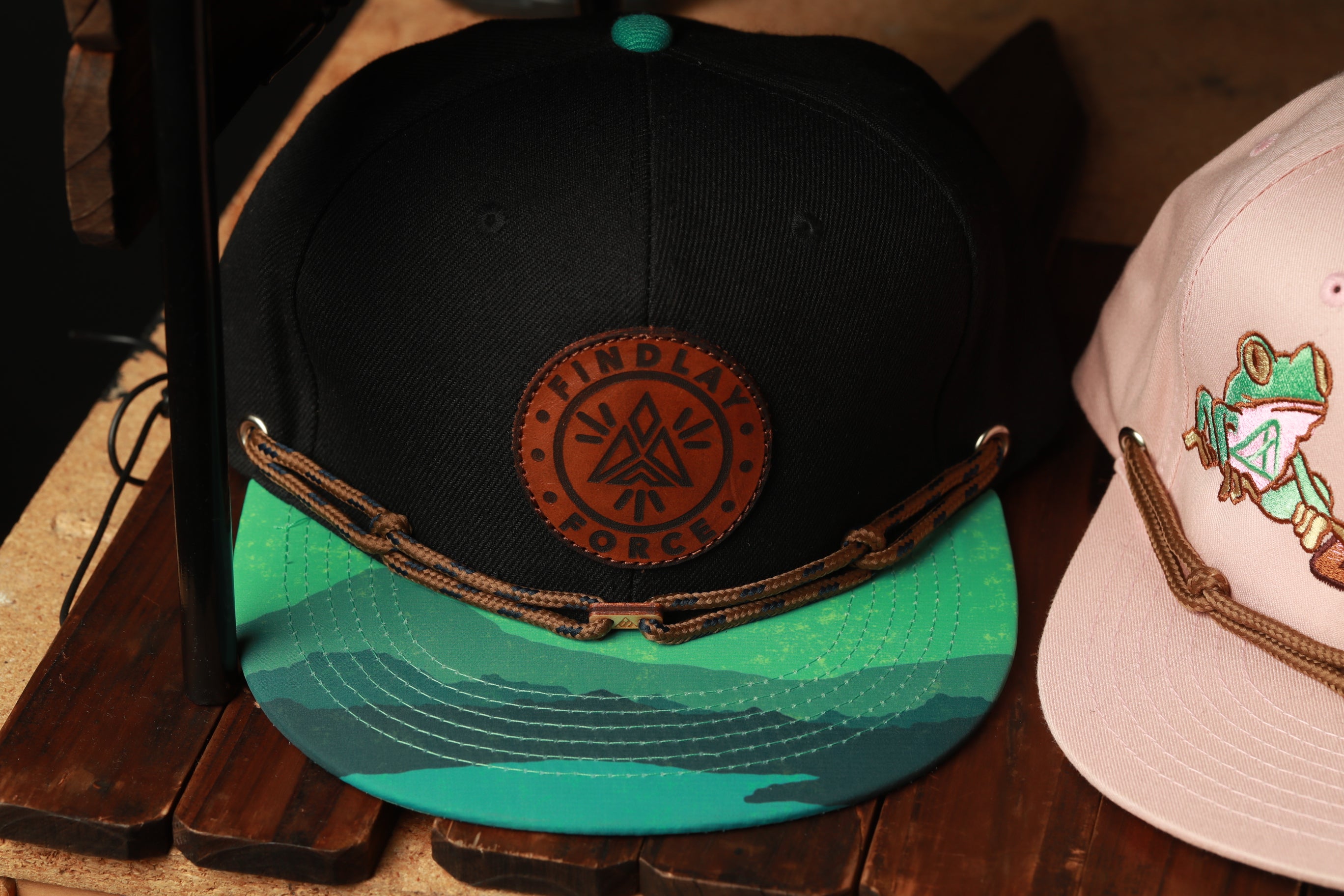 two baseball caps on a wooden surface, one black and one pink.