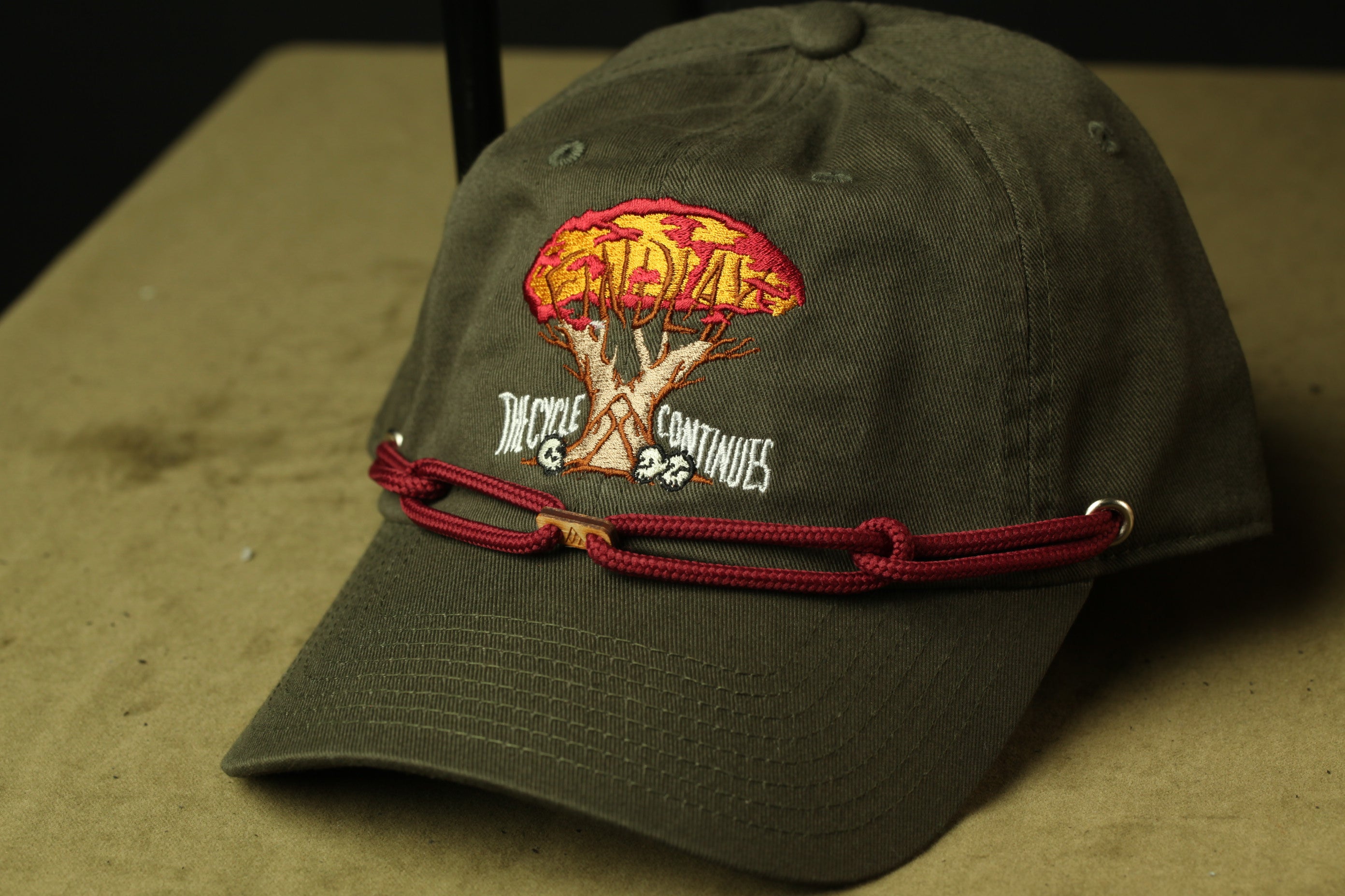A green baseball cap with a red string and an embroidered design on the front.